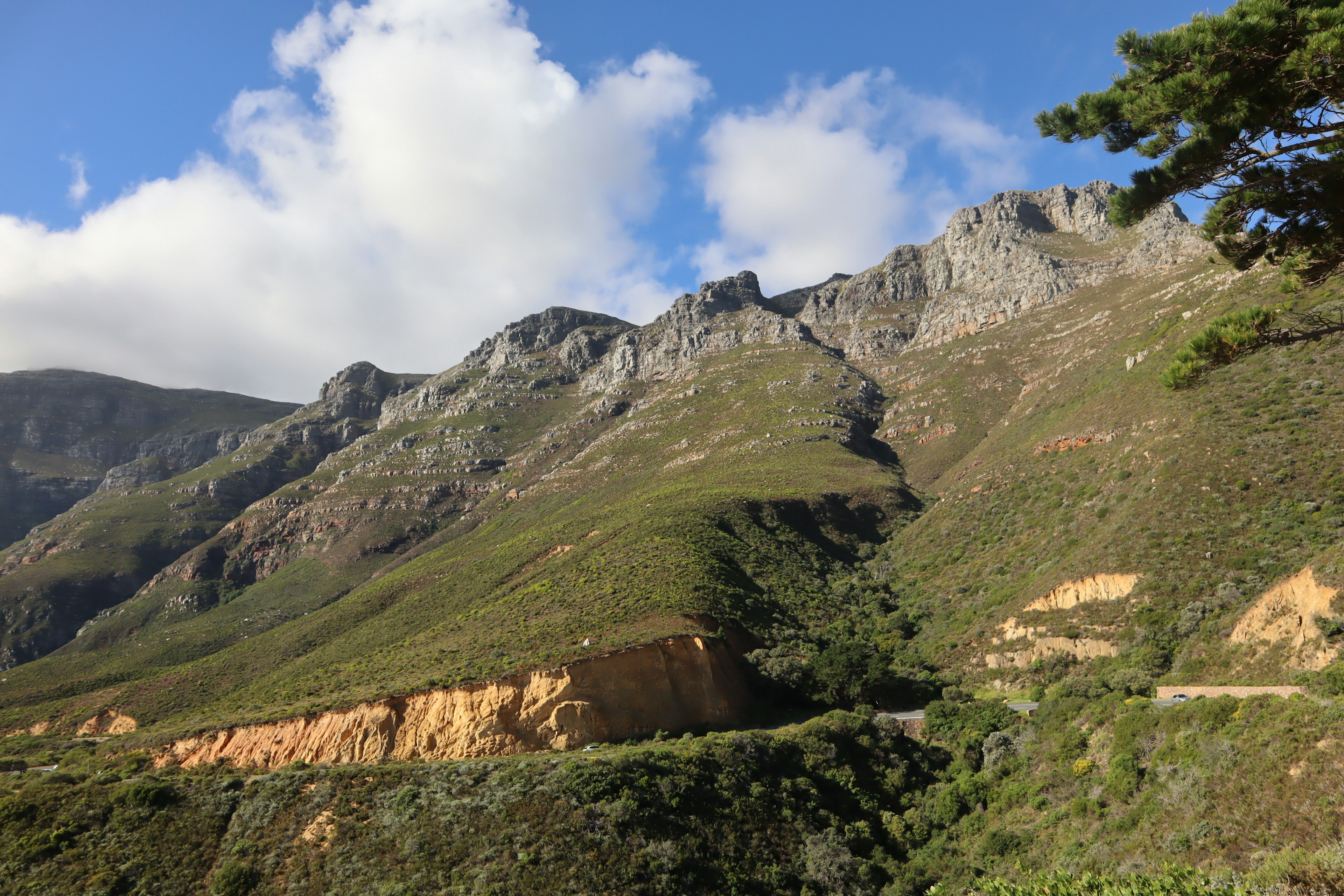 Lush green mountain landscape under blue sky featuring rocky slopes and clouds