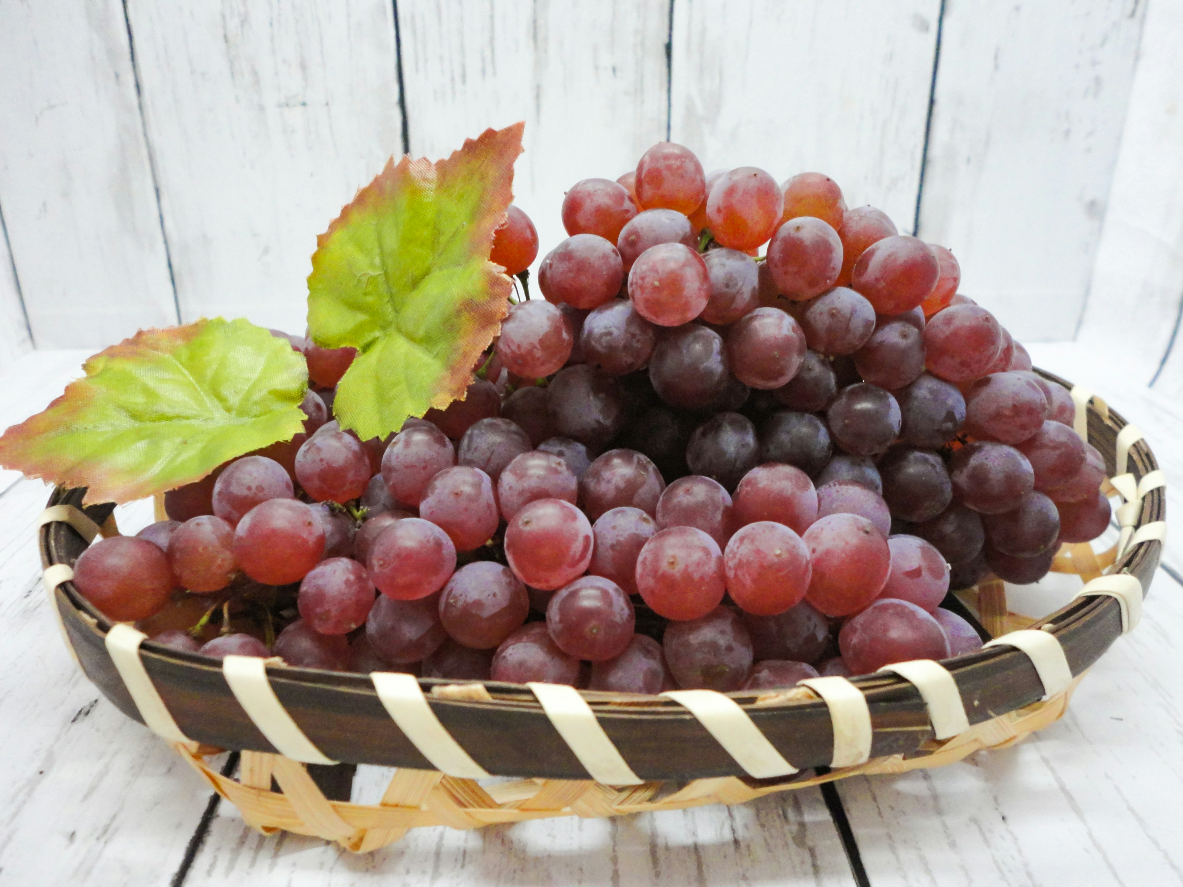 Red grapes in a woven basket with green leaves