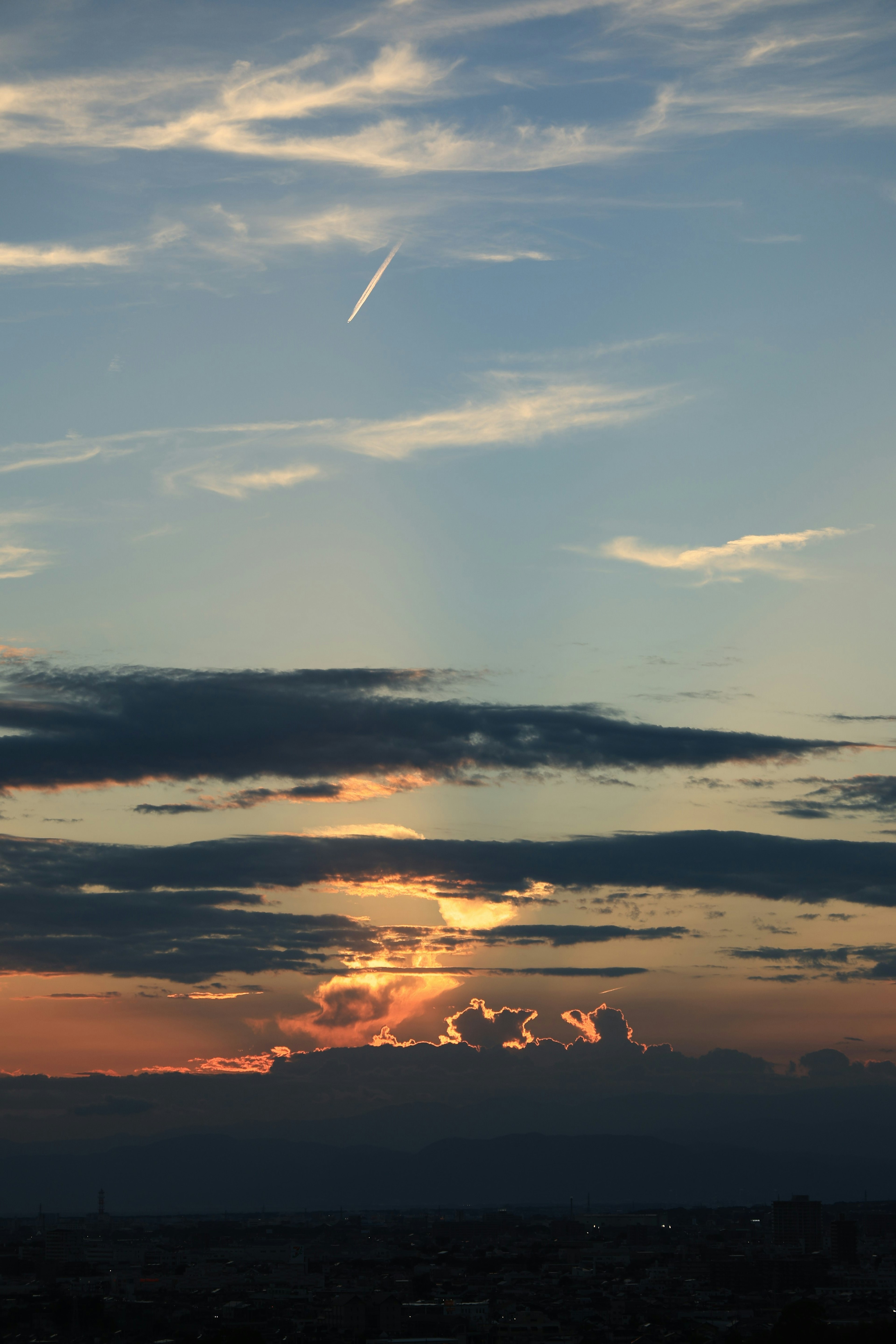 Ciel de coucher de soleil magnifique avec des couches de nuages et une traînée d'avion dans l'atmosphère supérieure