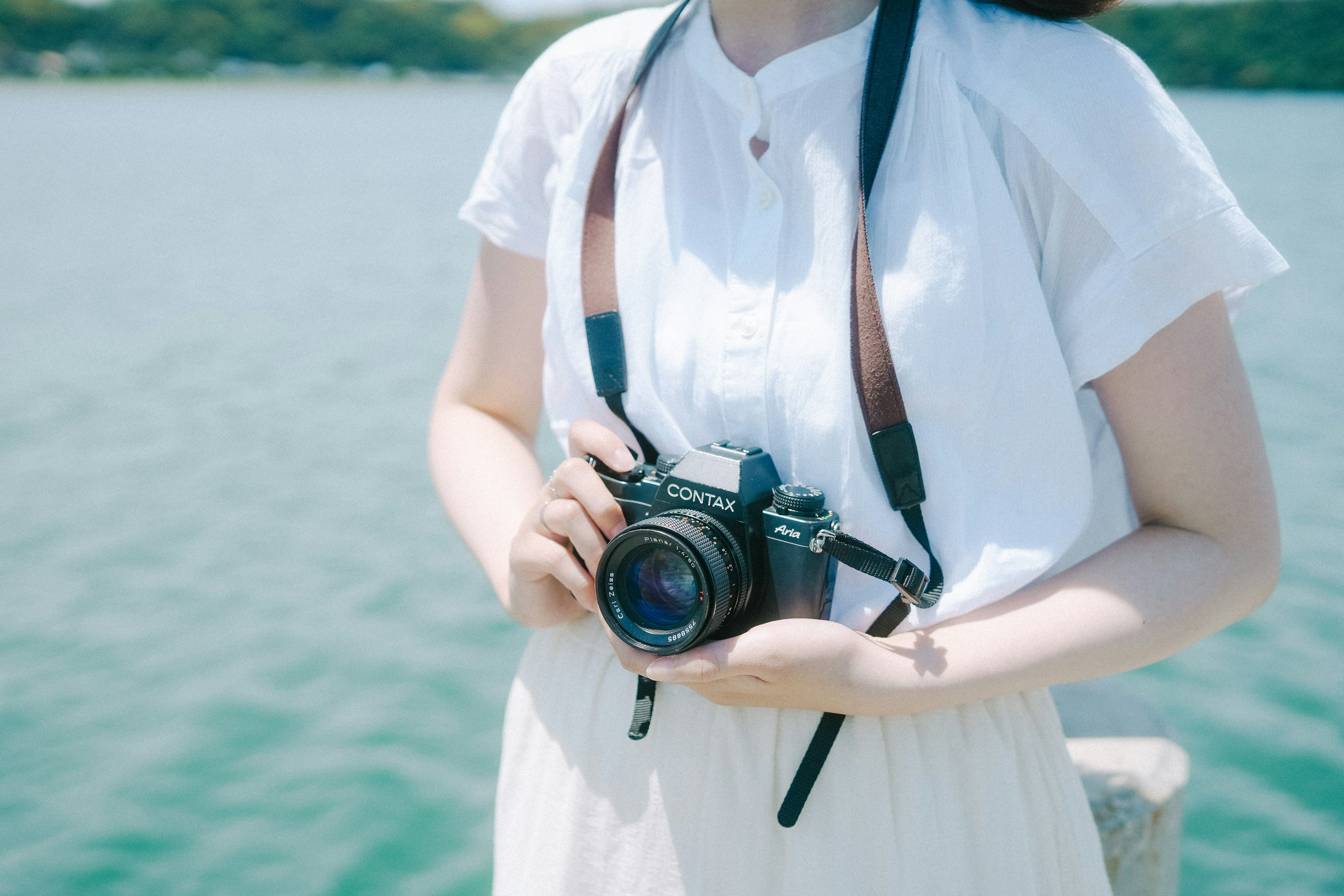 A woman holding a camera standing by the water