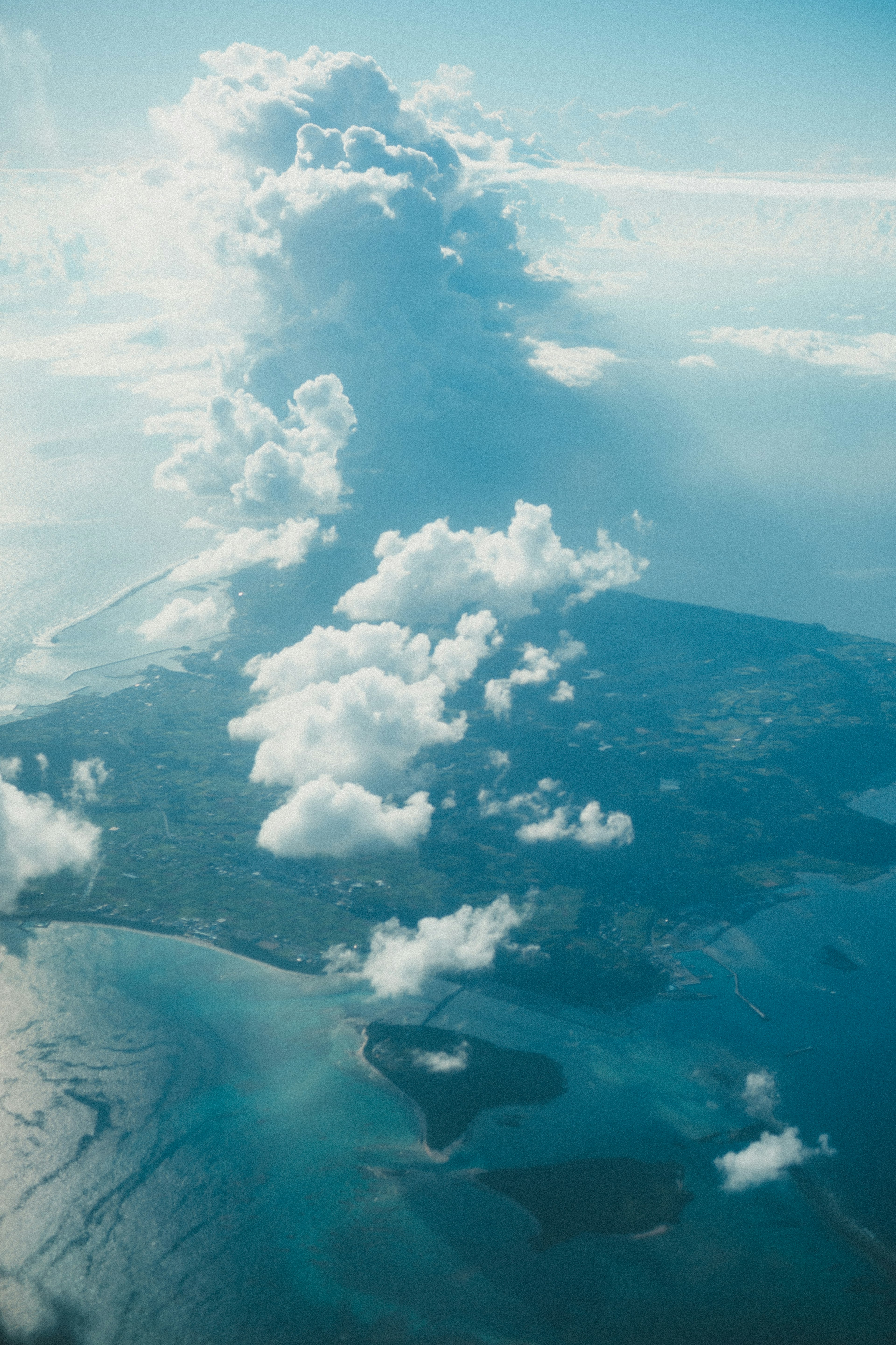 Aerial view of an island surrounded by blue waters and clouds