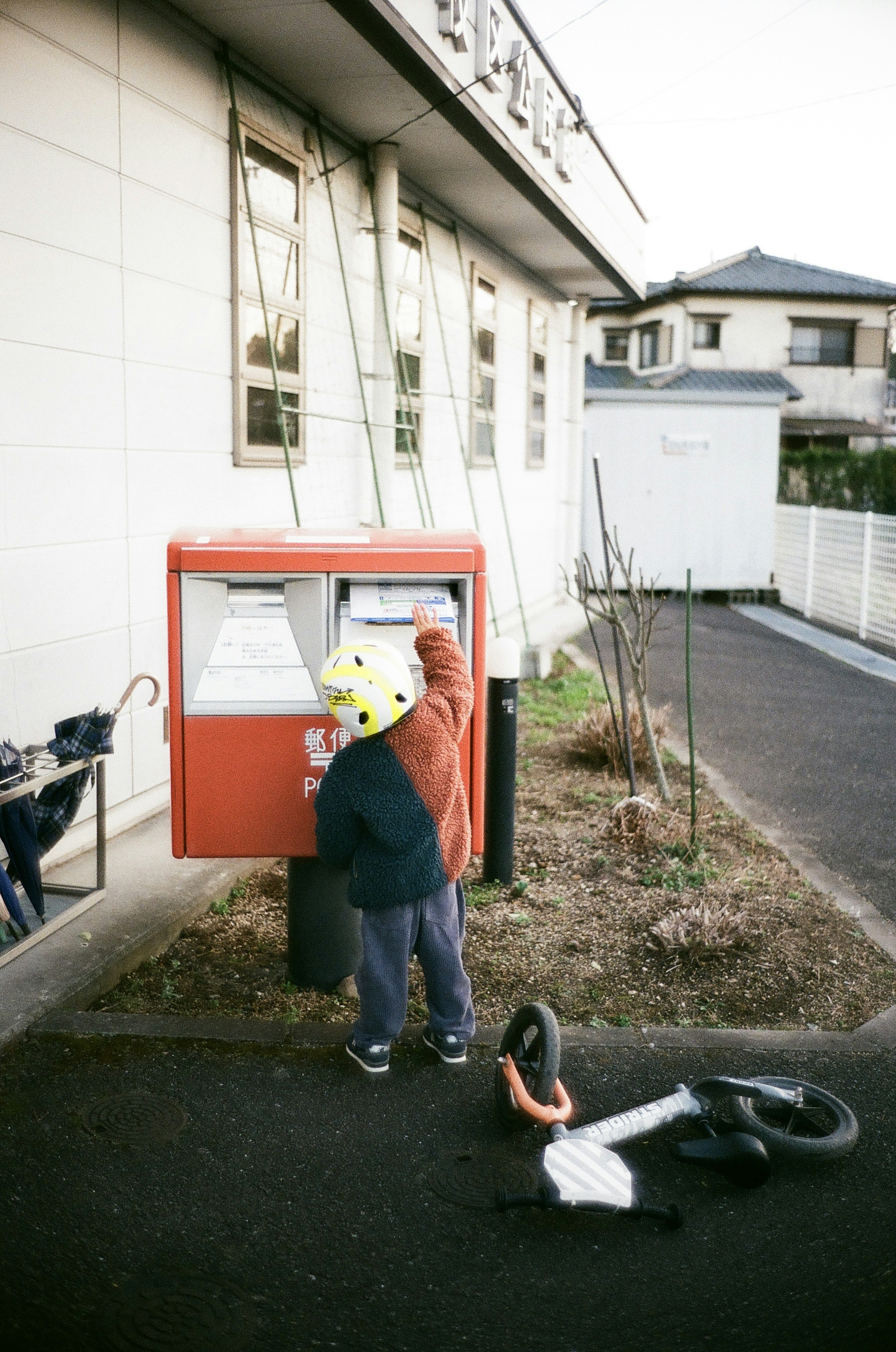 A child placing a letter into a mailbox with a bicycle nearby