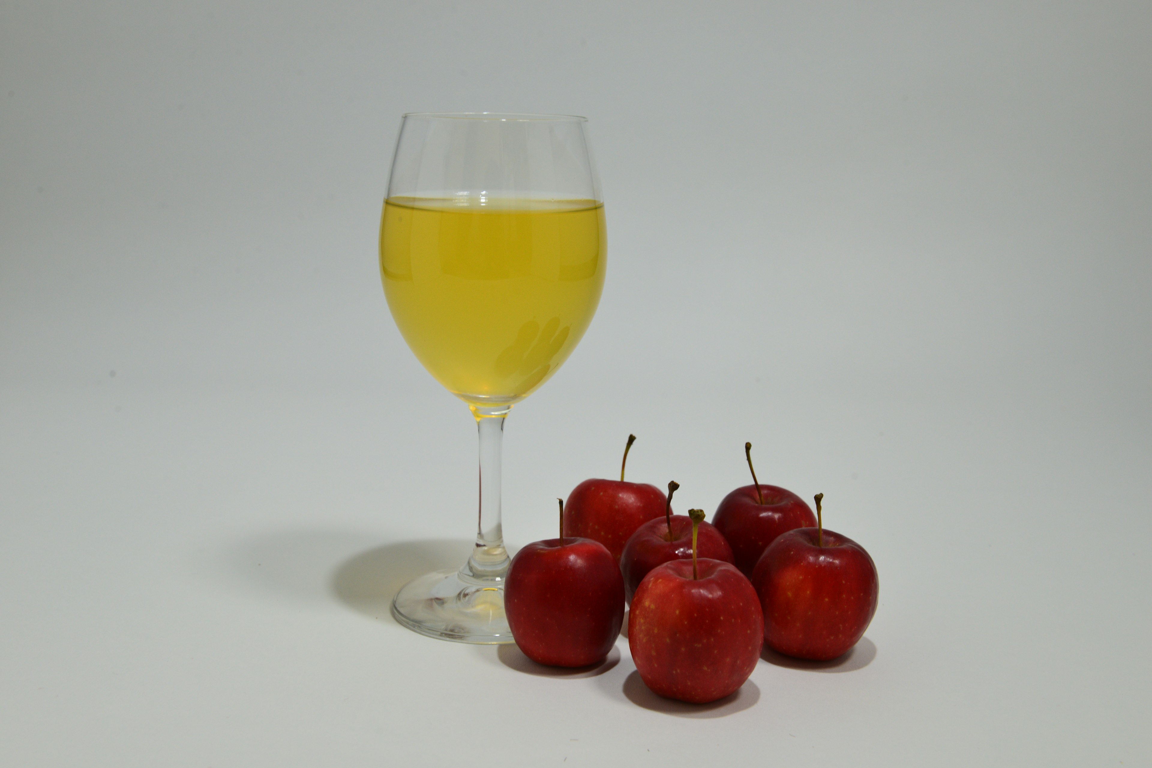 A transparent glass filled with yellow drink next to a cluster of red apples in a simple still life