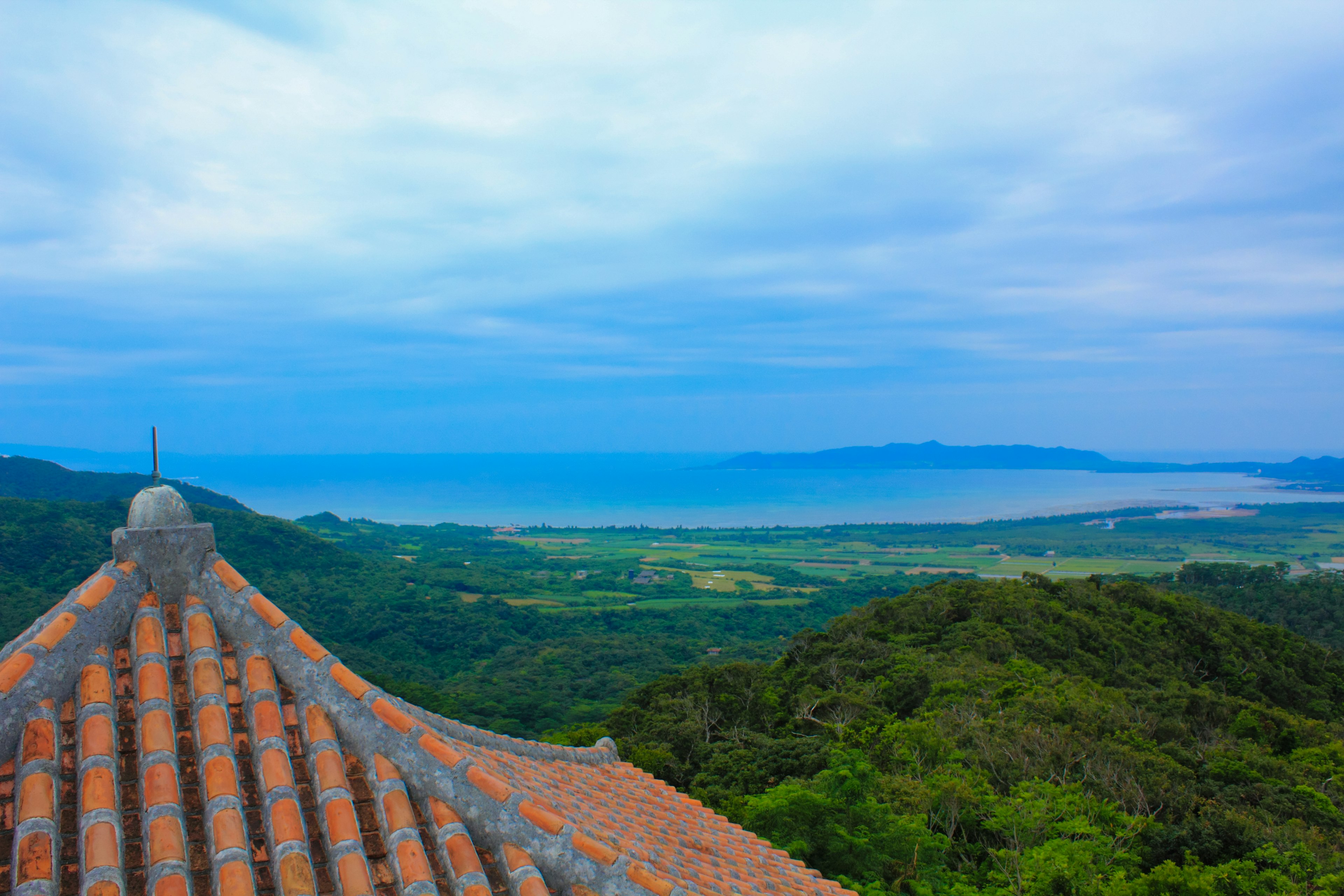 View of a tiled roof with blue sky and ocean in the background green hills and fields visible