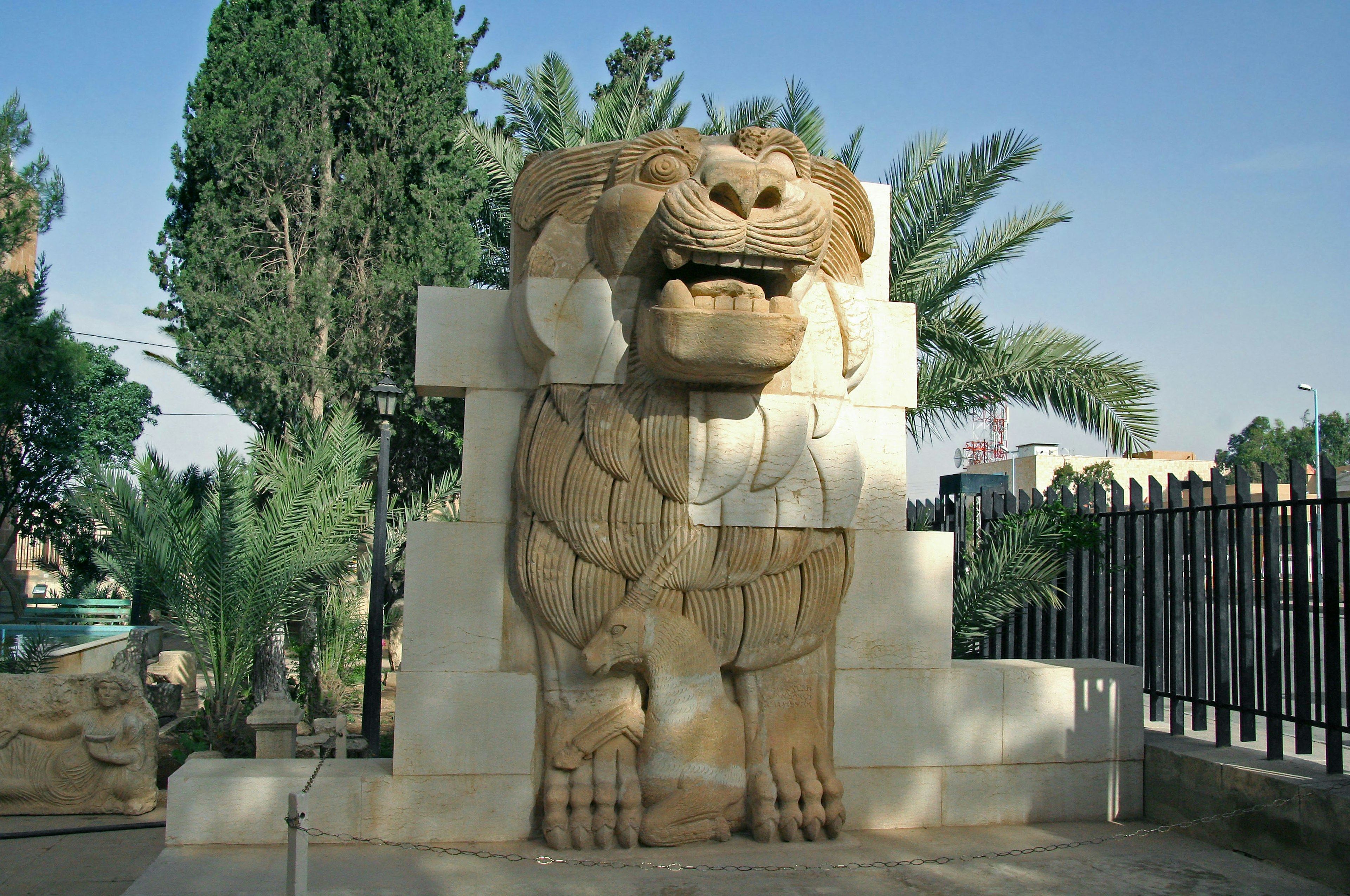 Sculpture de lion en pierre dans un parc avec des arbres verts et un ciel bleu en arrière-plan