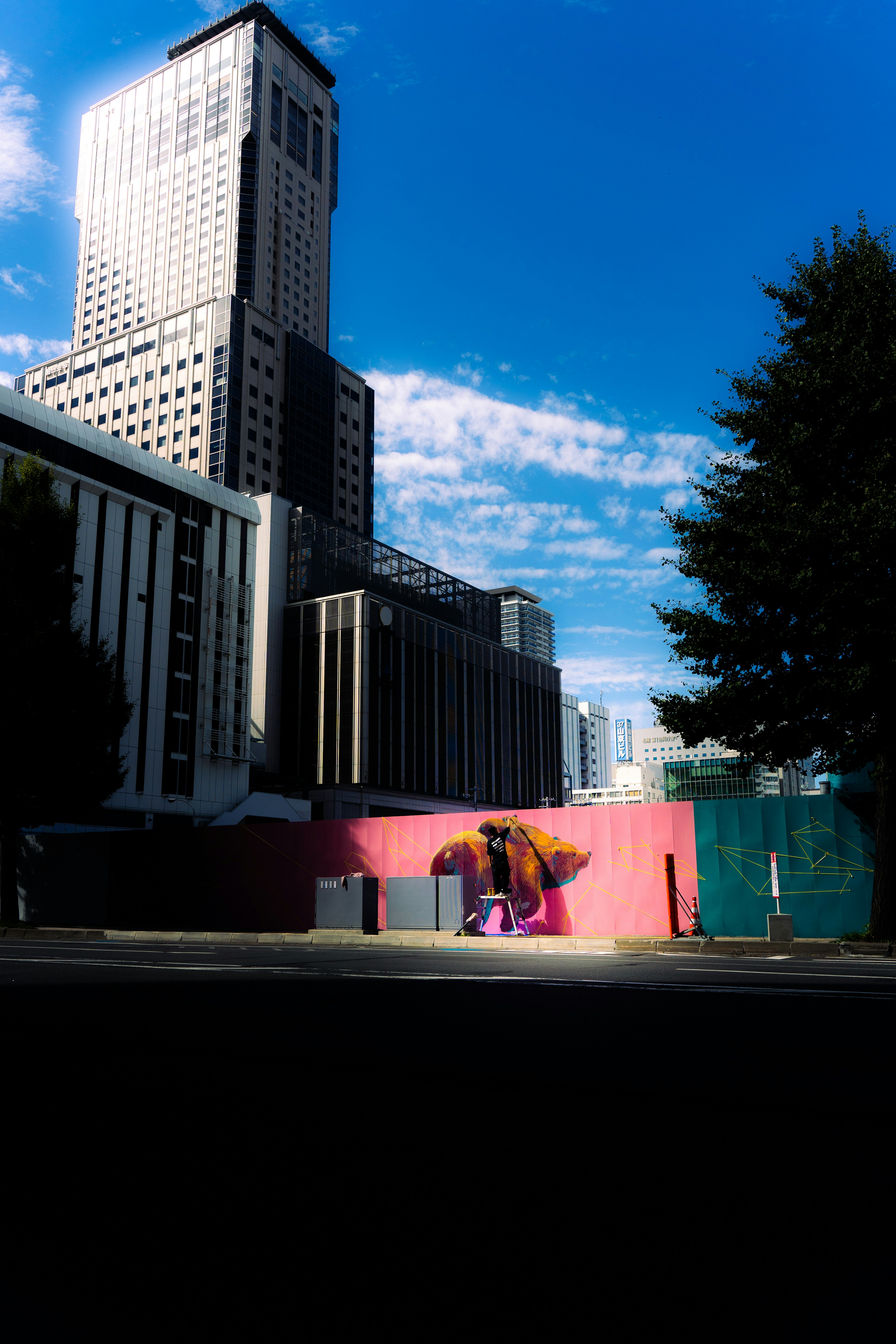 Personne assise contre un mur rose sous un ciel bleu avec des gratte-ciel