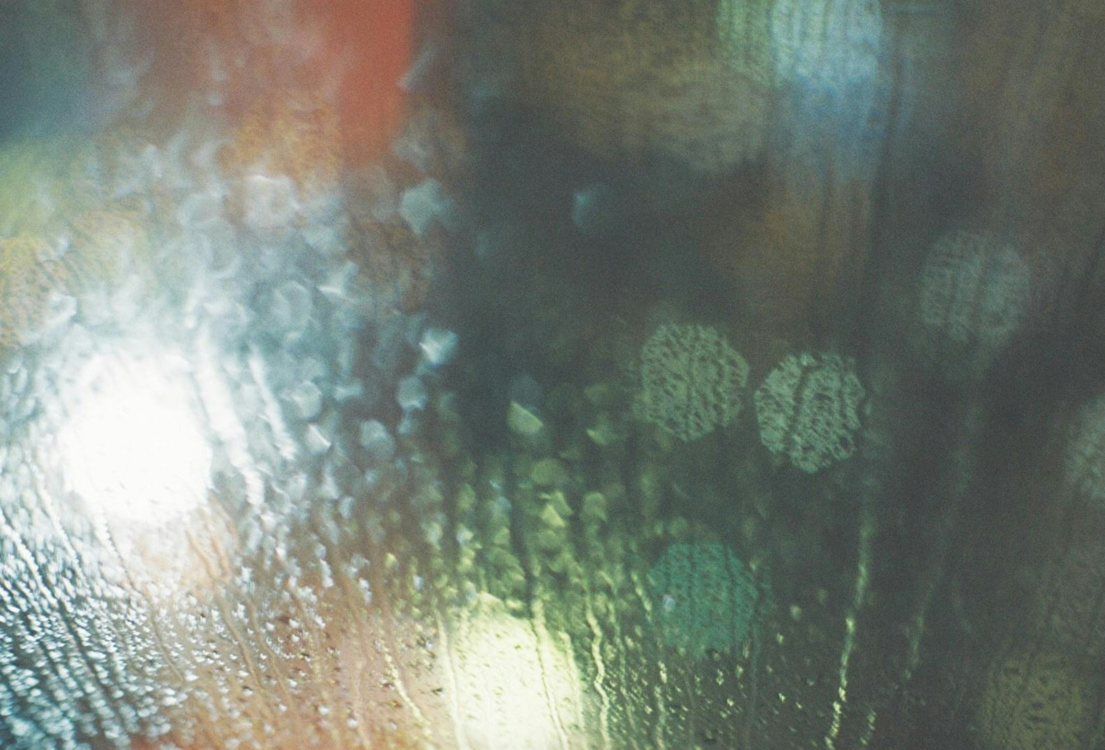 Close-up of a window with blurred lights and water droplets