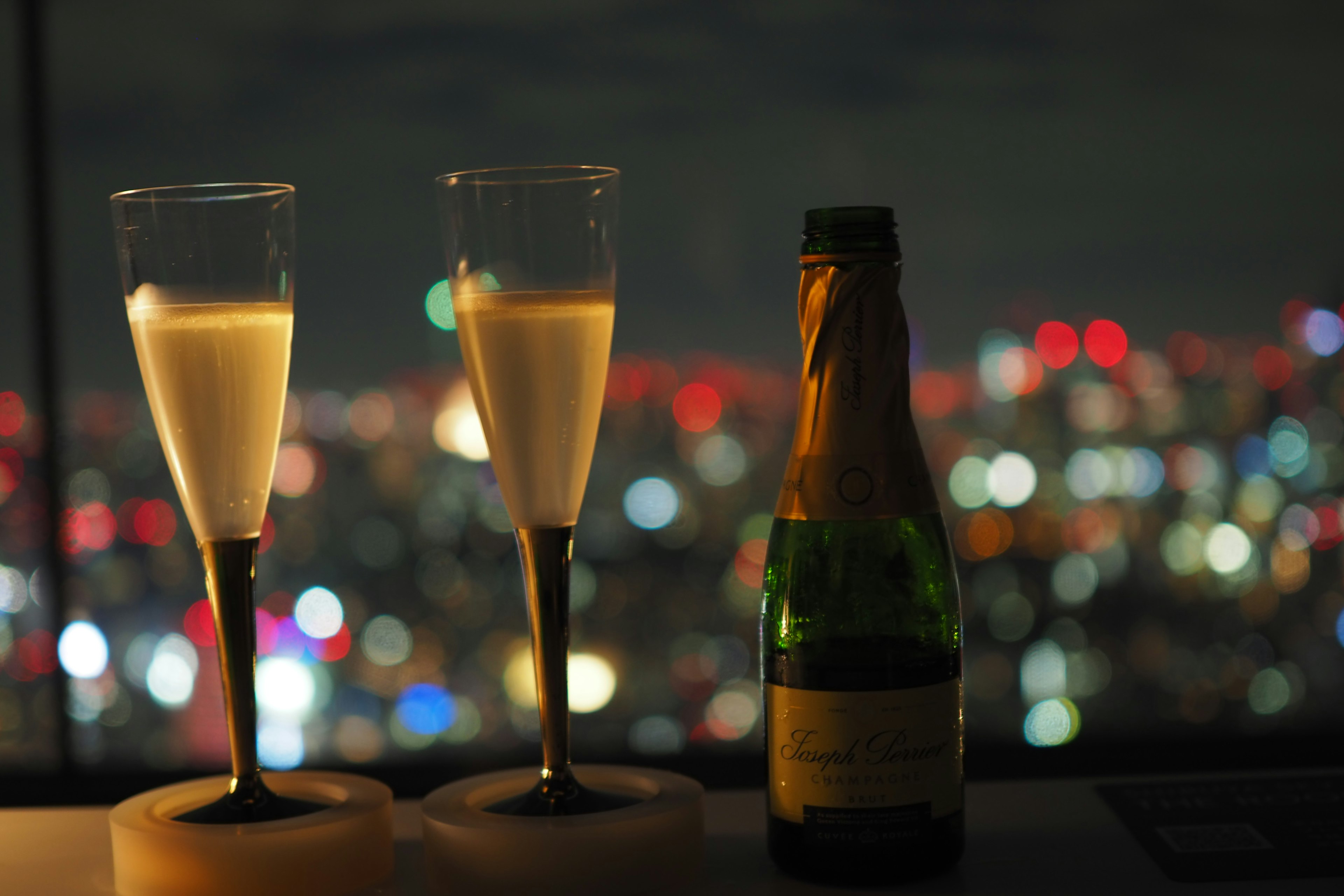 Dos copas de champán y una botella con fondo de ciudad nocturna