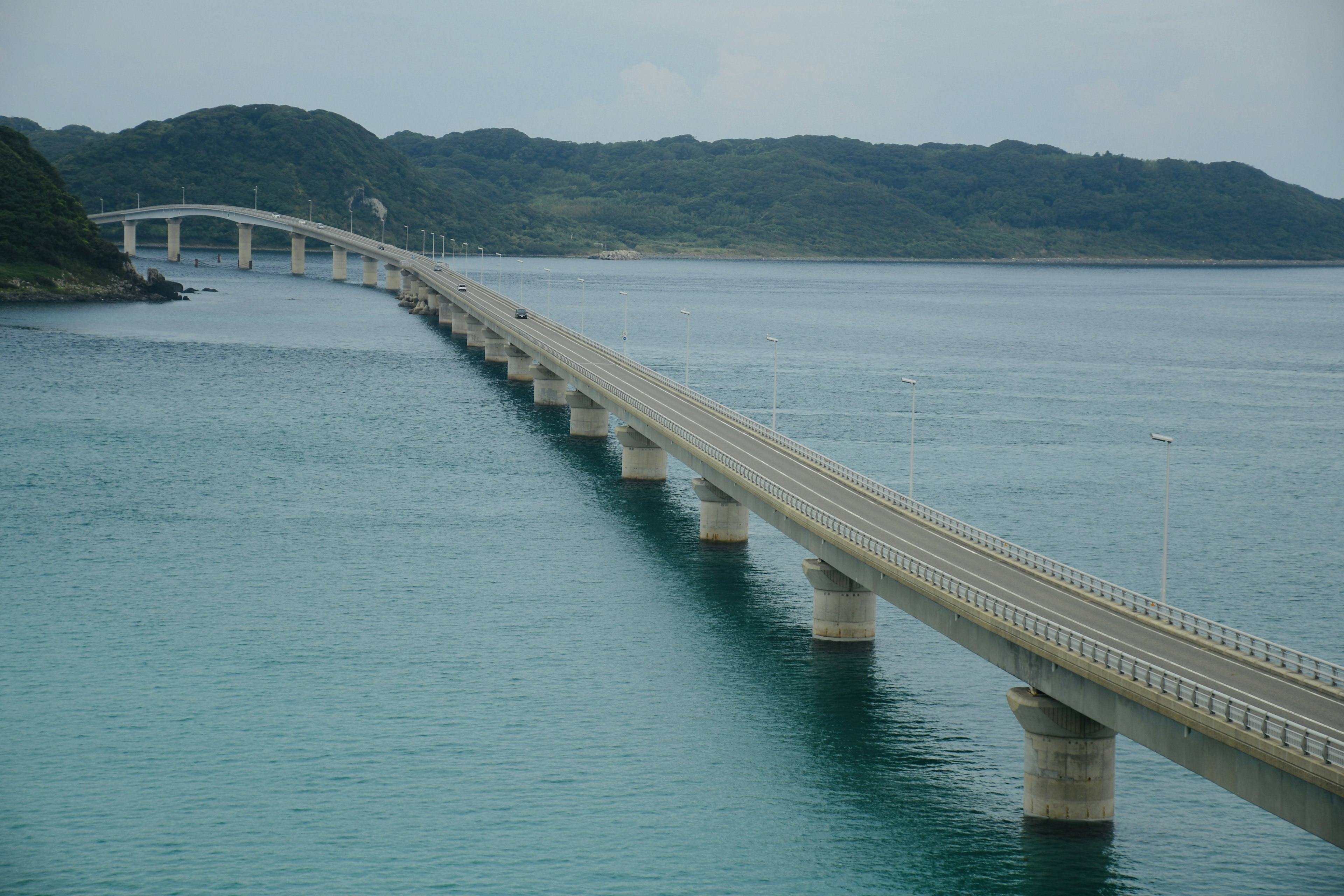 A long bridge over blue water with green islands in the background