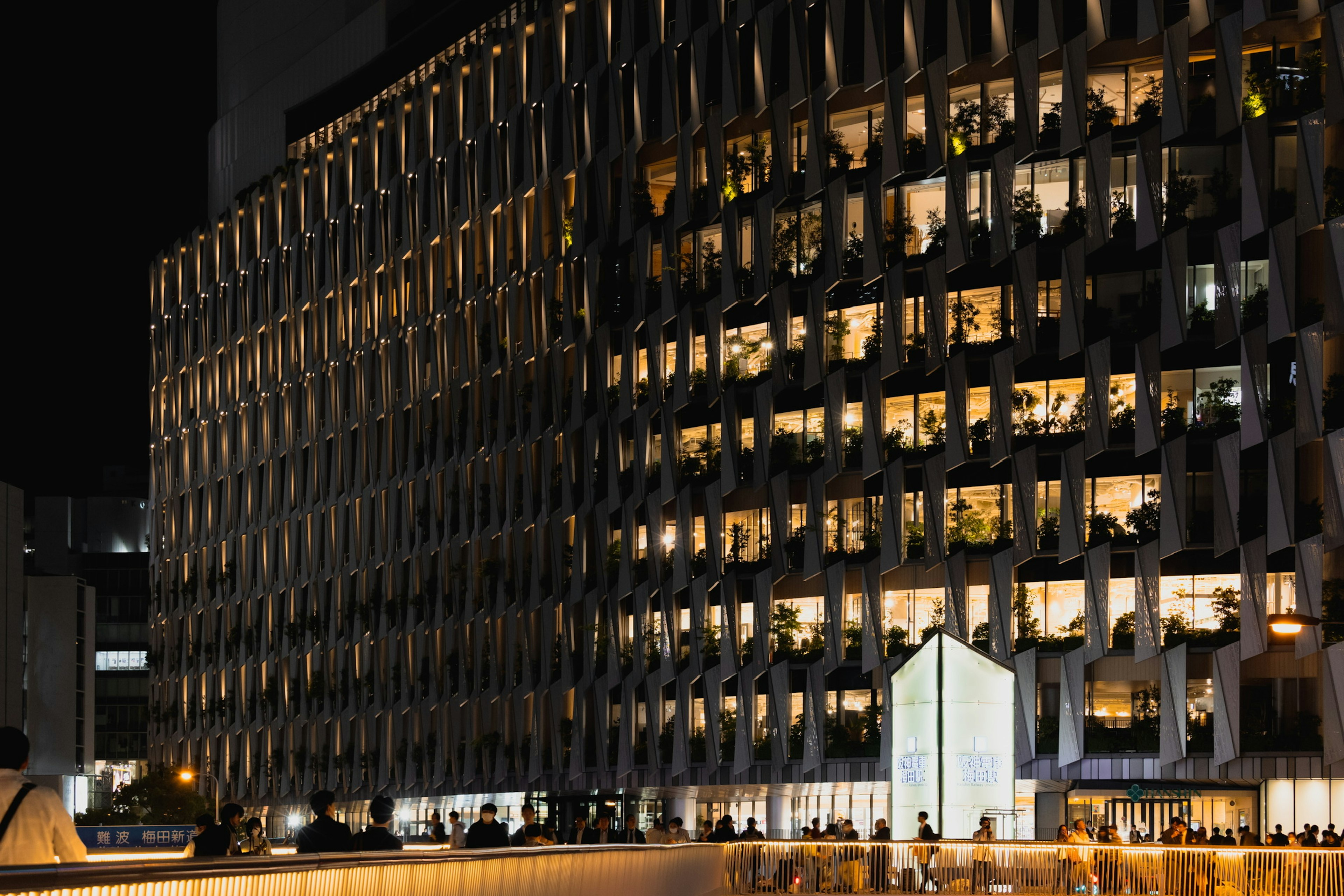 Eksterior gedung kantor yang diterangi di malam hari dengan jendela terang dan desain modern