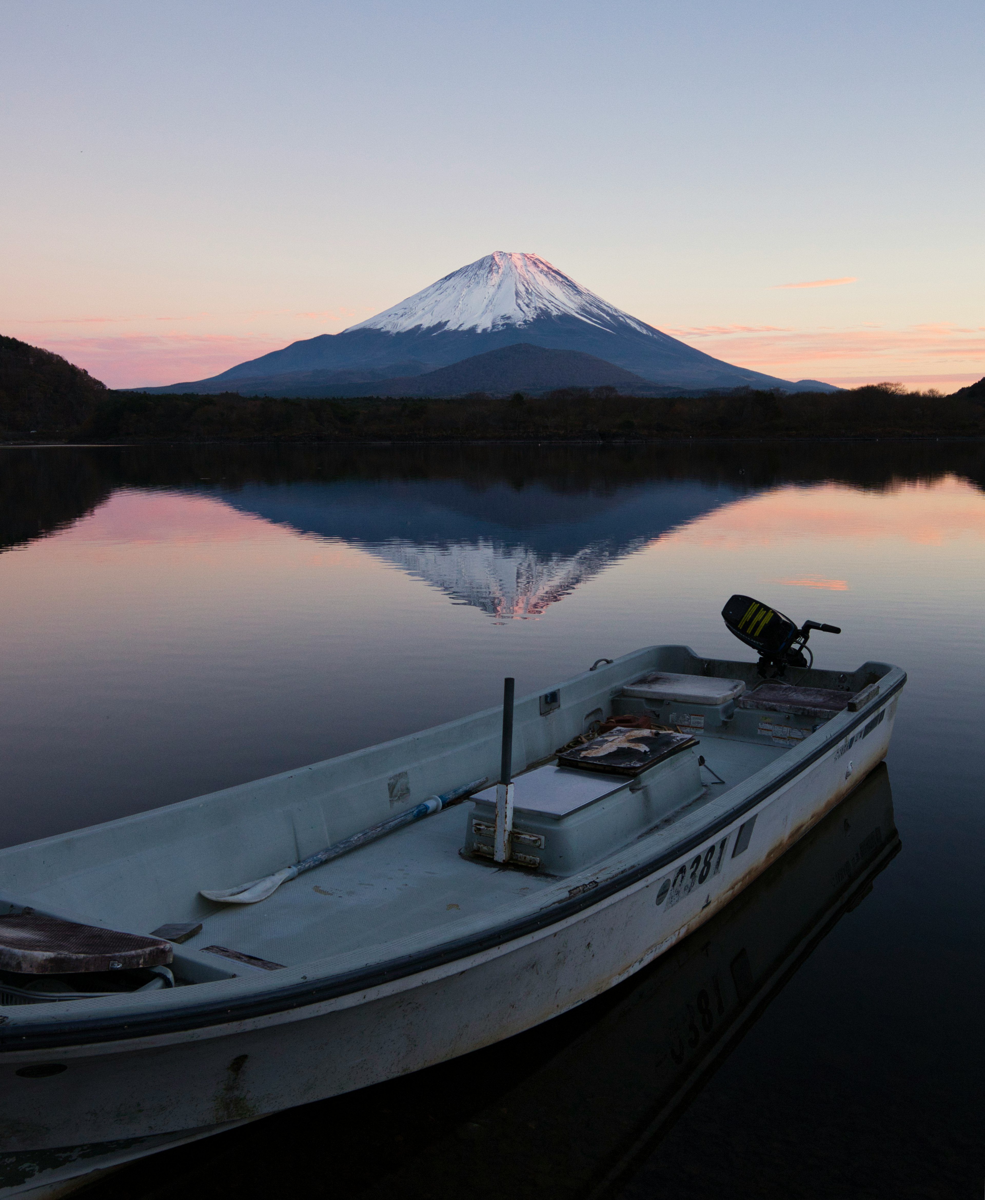 Sebuah perahu kecil di danau tenang yang memantulkan Gunung Fuji saat matahari terbenam