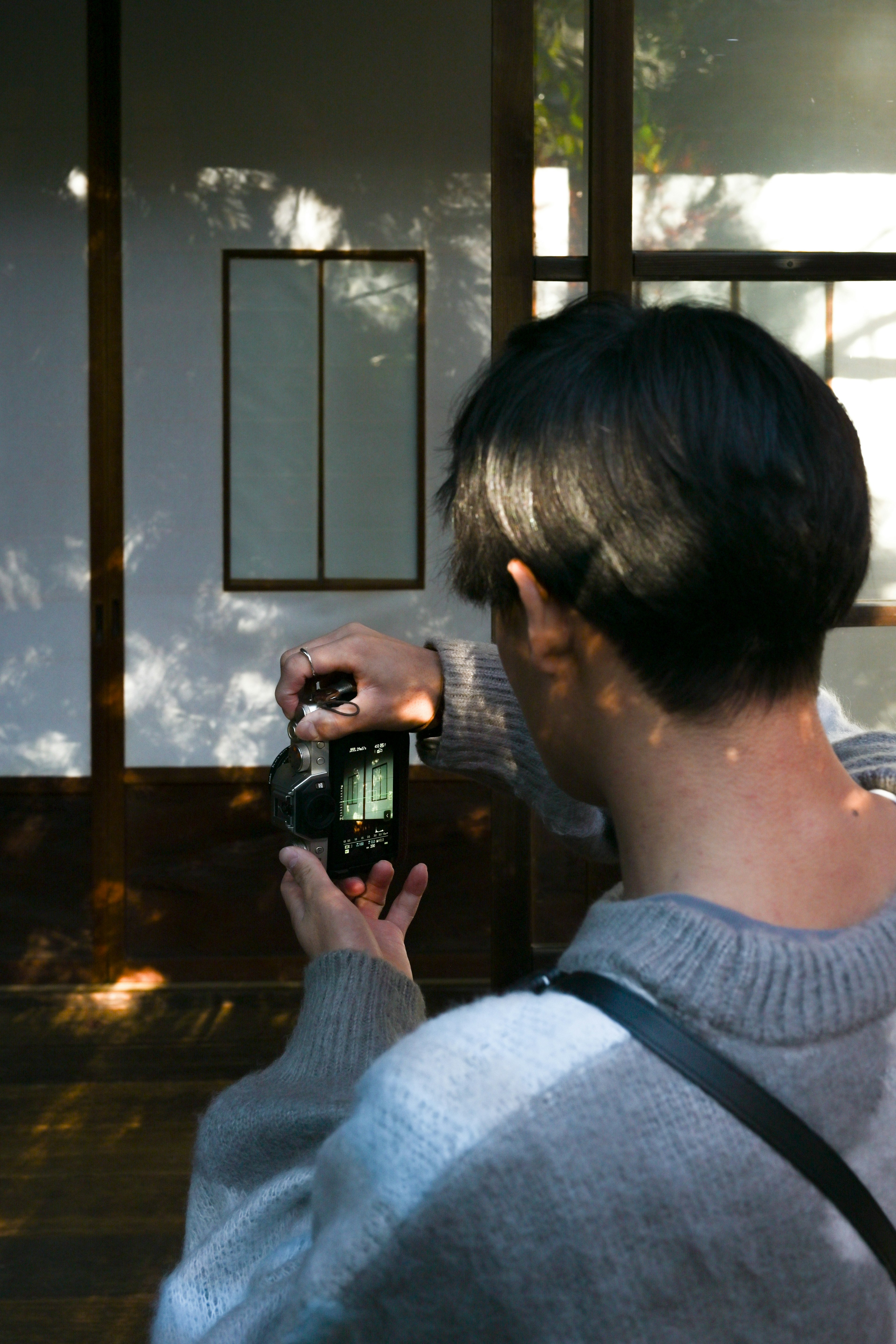 A young person taking a photo with a camera in front of a simple Japanese room wall with light patterns