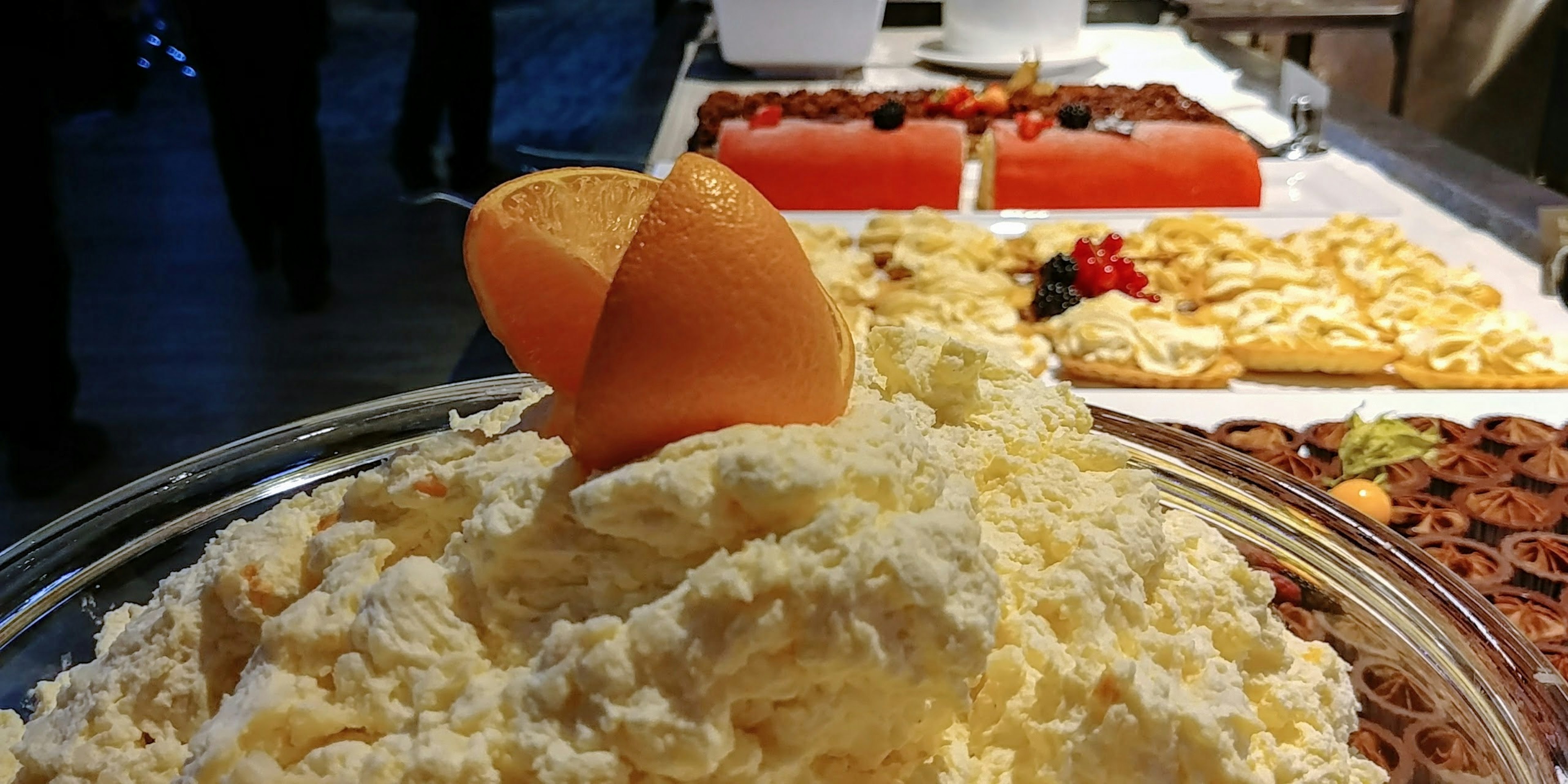 Un dessert crémeux surmonté d'une tranche d'orange avec divers desserts en arrière-plan