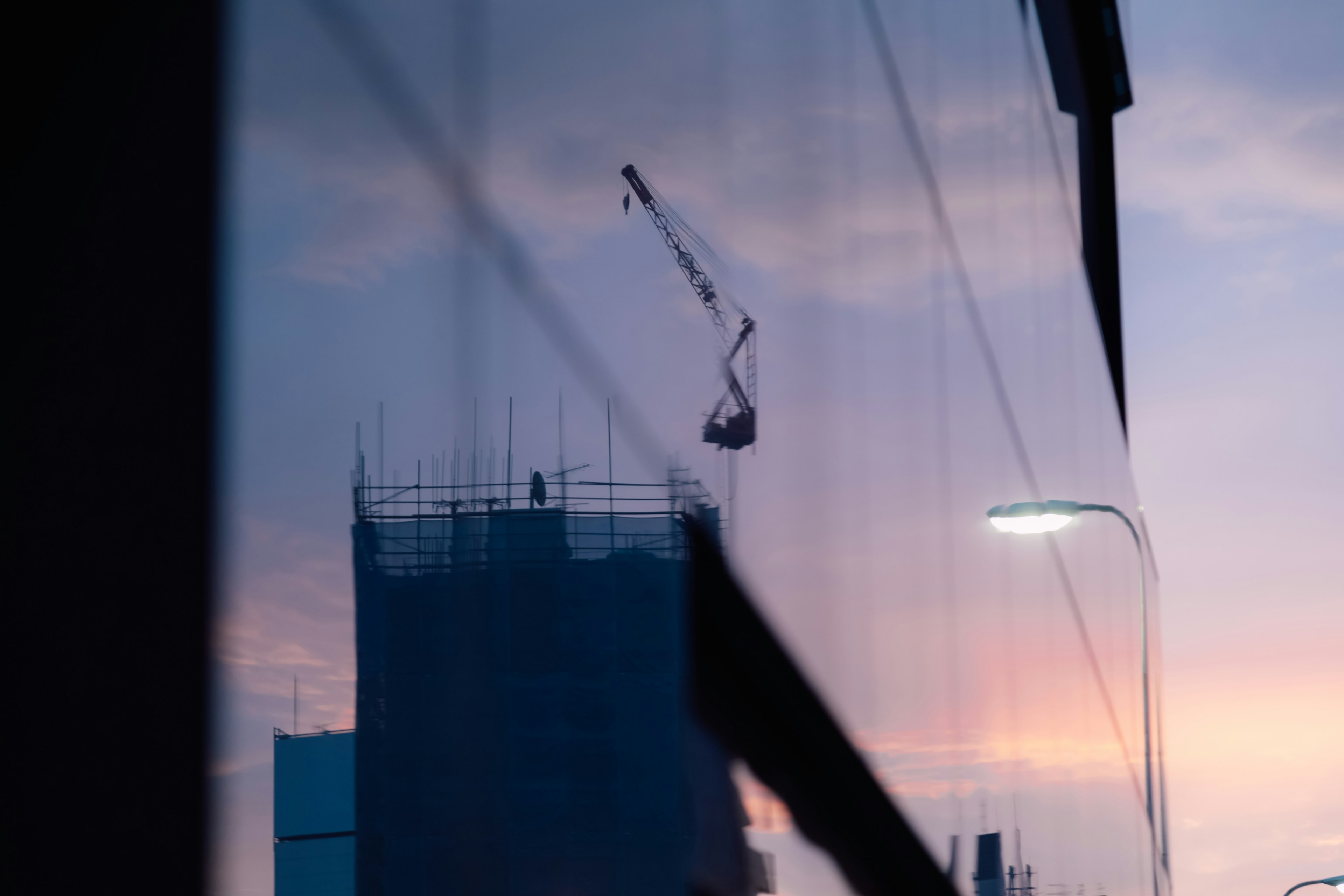 Reflejo de una grúa y un edificio en construcción en una ventana con fondo de atardecer