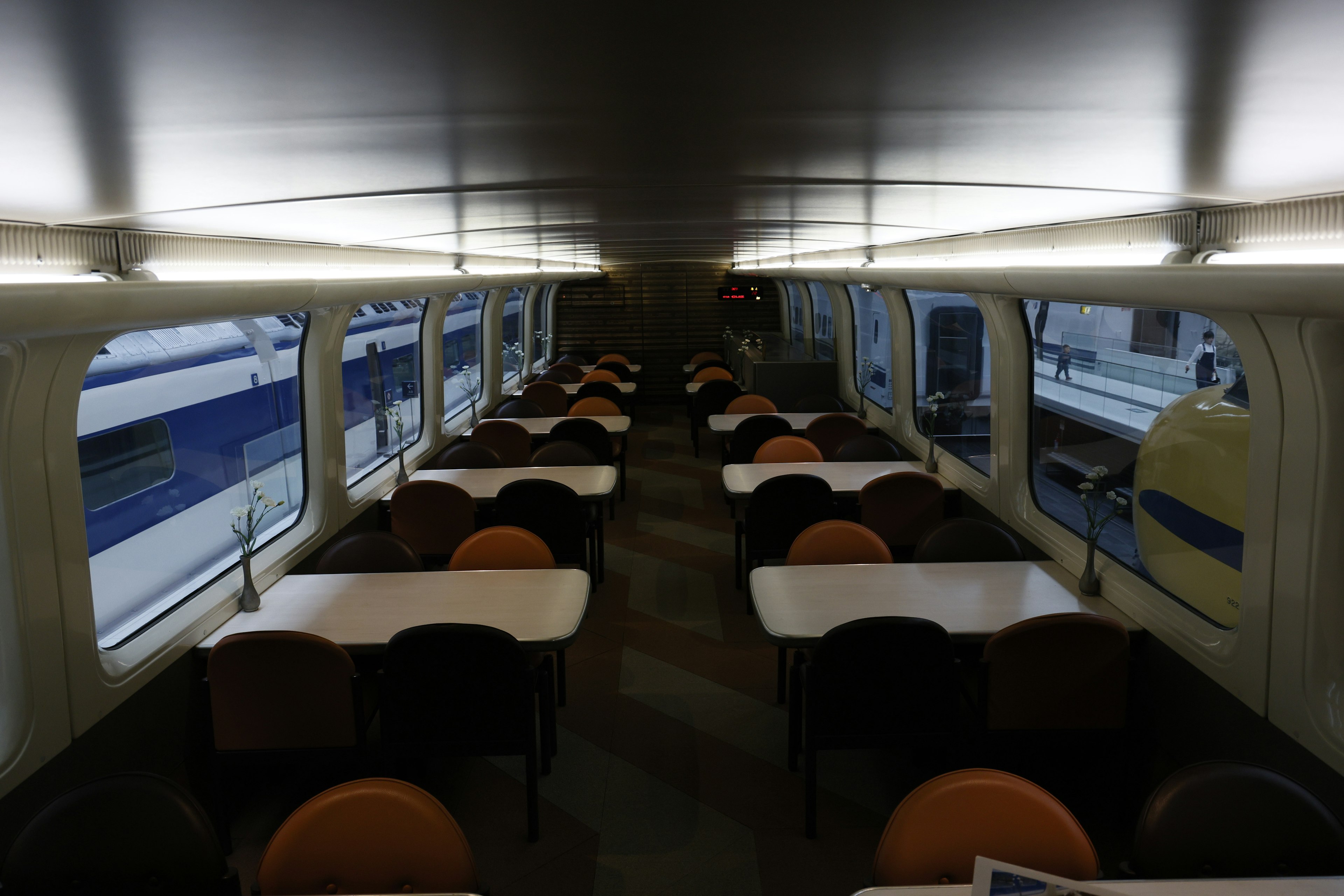 Interior of a train carriage featuring long tables and chairs resembling a dining area