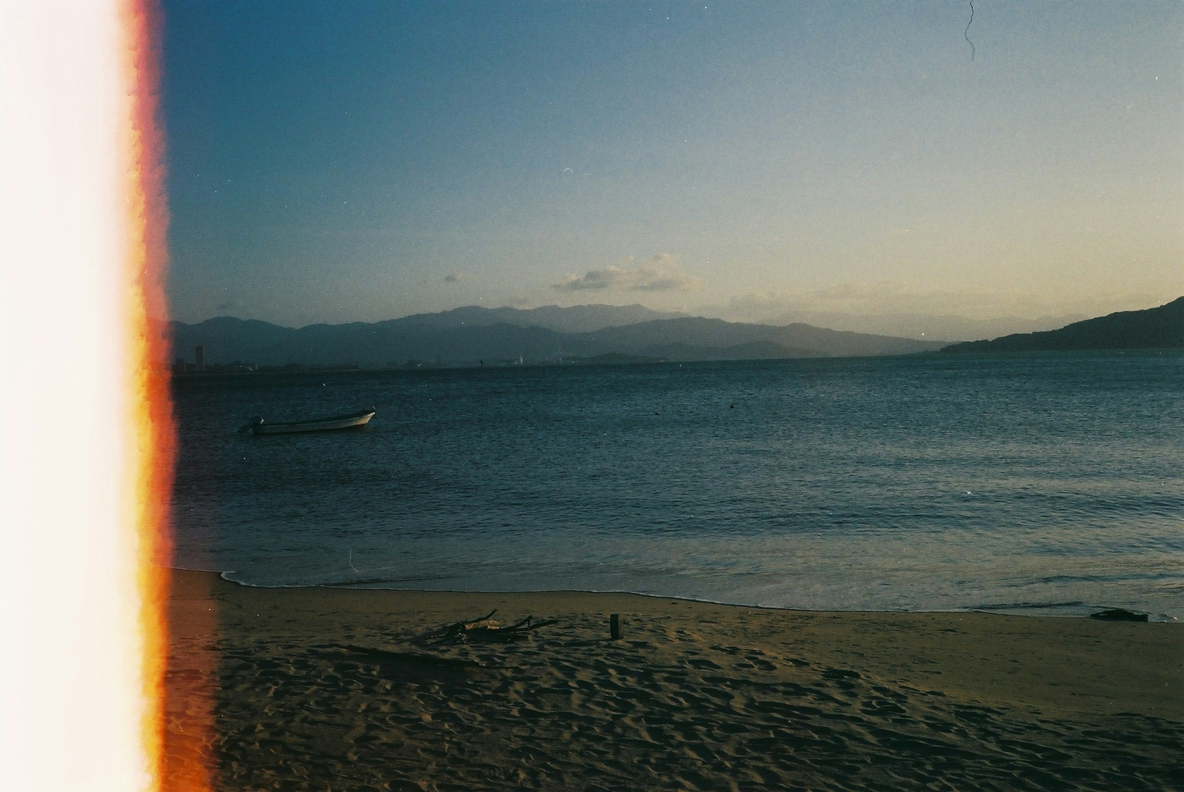 Playa al atardecer con montañas de fondo y un bote en el agua