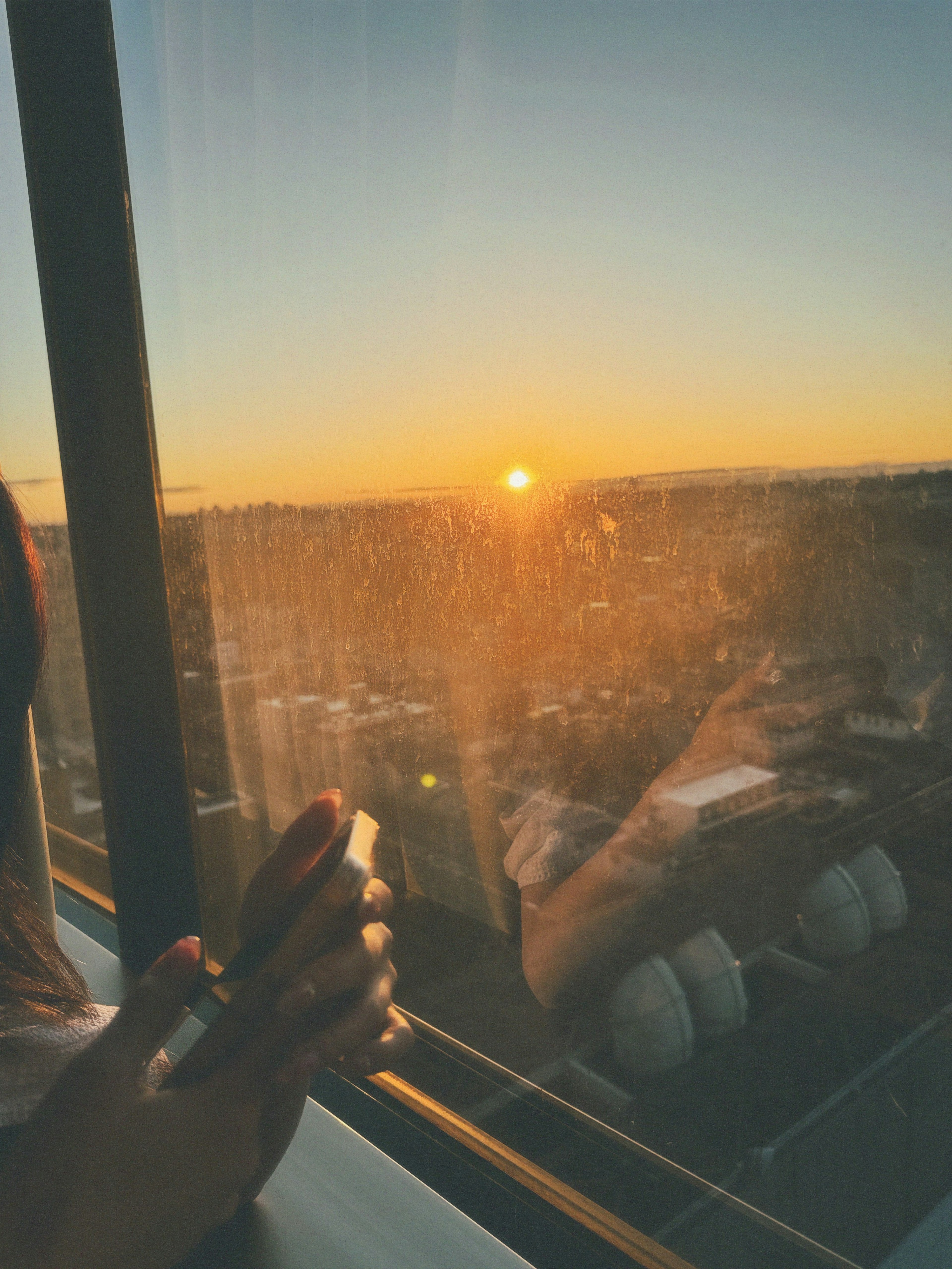 Silhouette d'une main tenant un téléphone près de la fenêtre avec vue sur le coucher de soleil