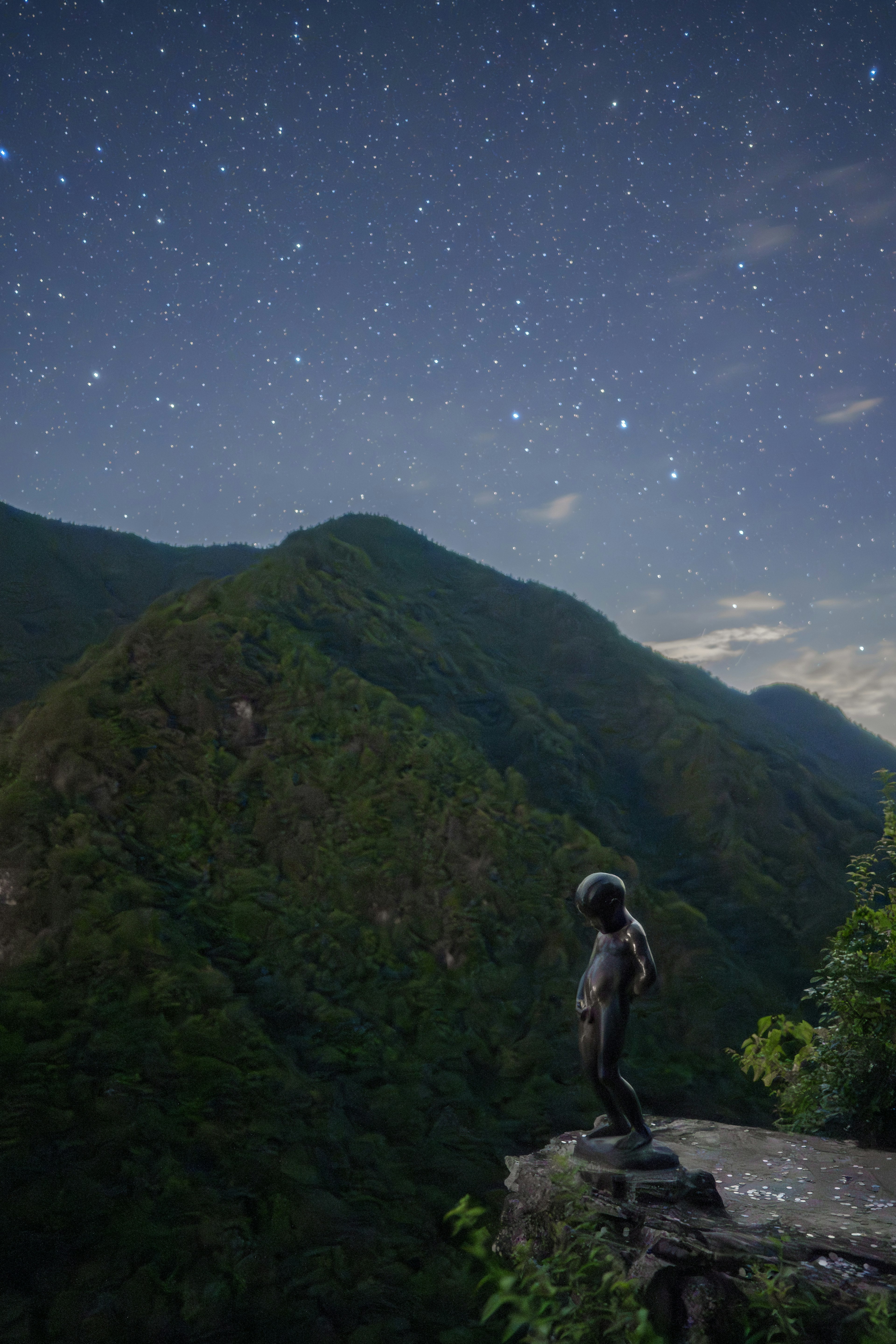 Statue of a boy standing on a mountain edge under a starry sky