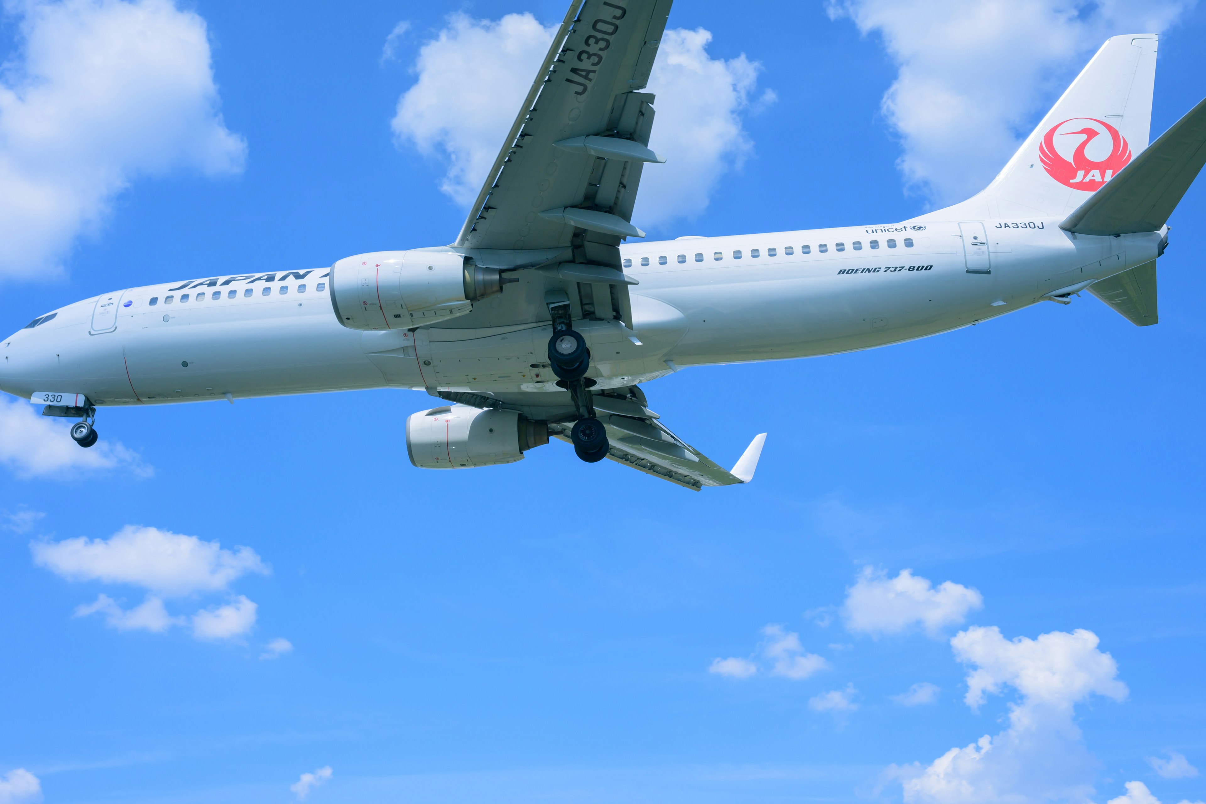 Avión volando contra un cielo azul con nubes blancas que presenta un logo rojo