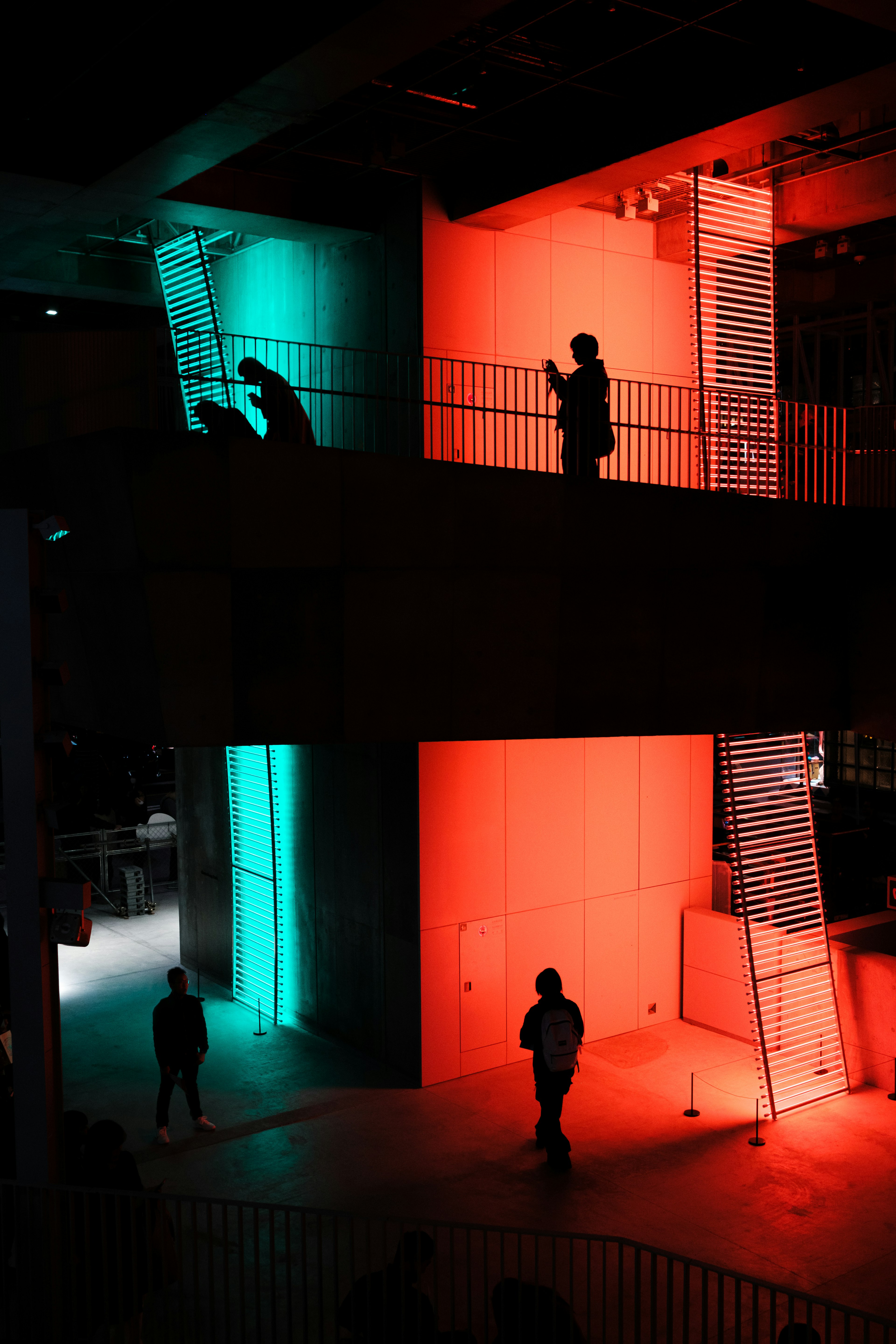 Silhouettes of people against vibrant blue and red lighting in a modern architectural space