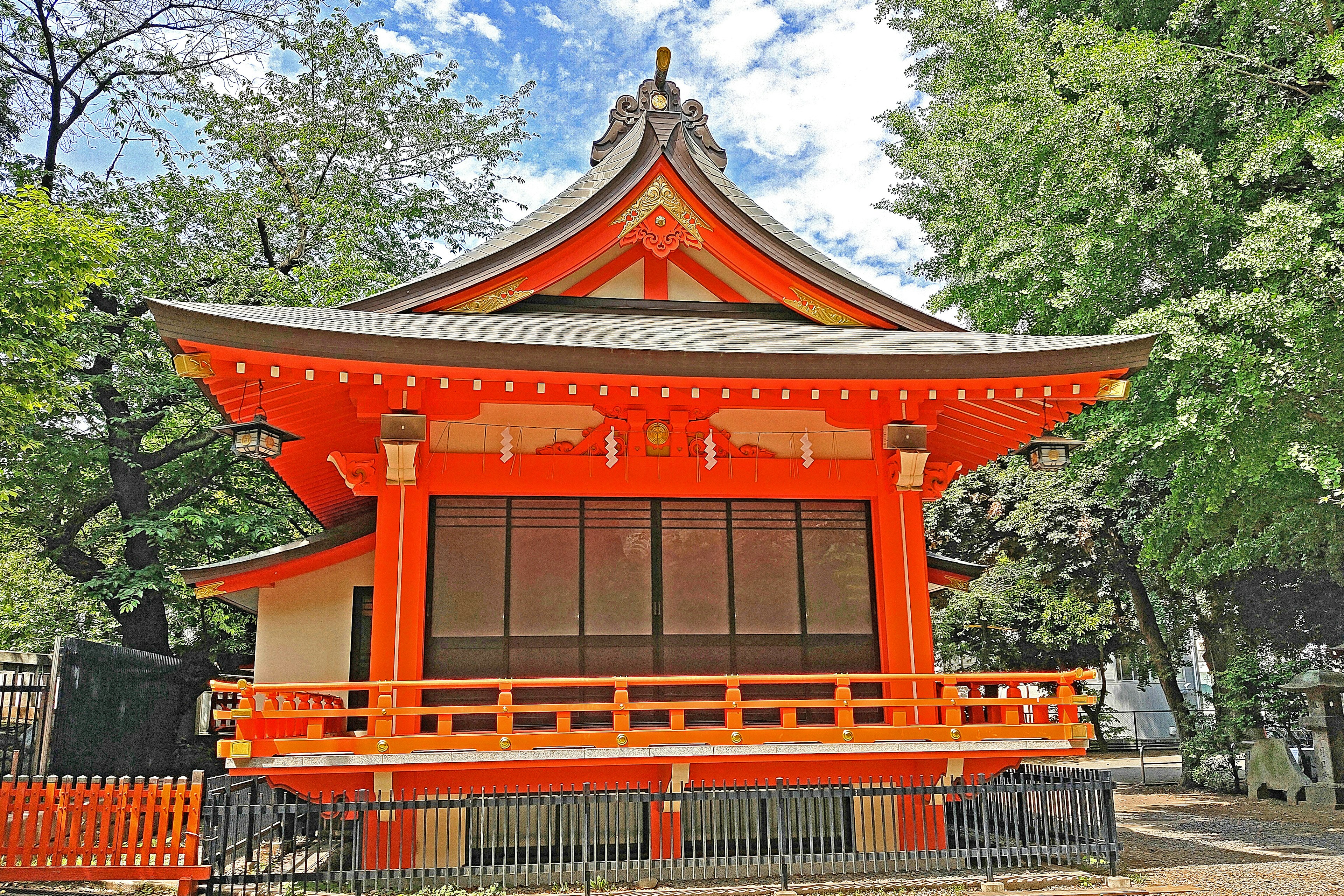 鮮やかなオレンジ色の神社の建物 青空と緑の木々に囲まれた風景