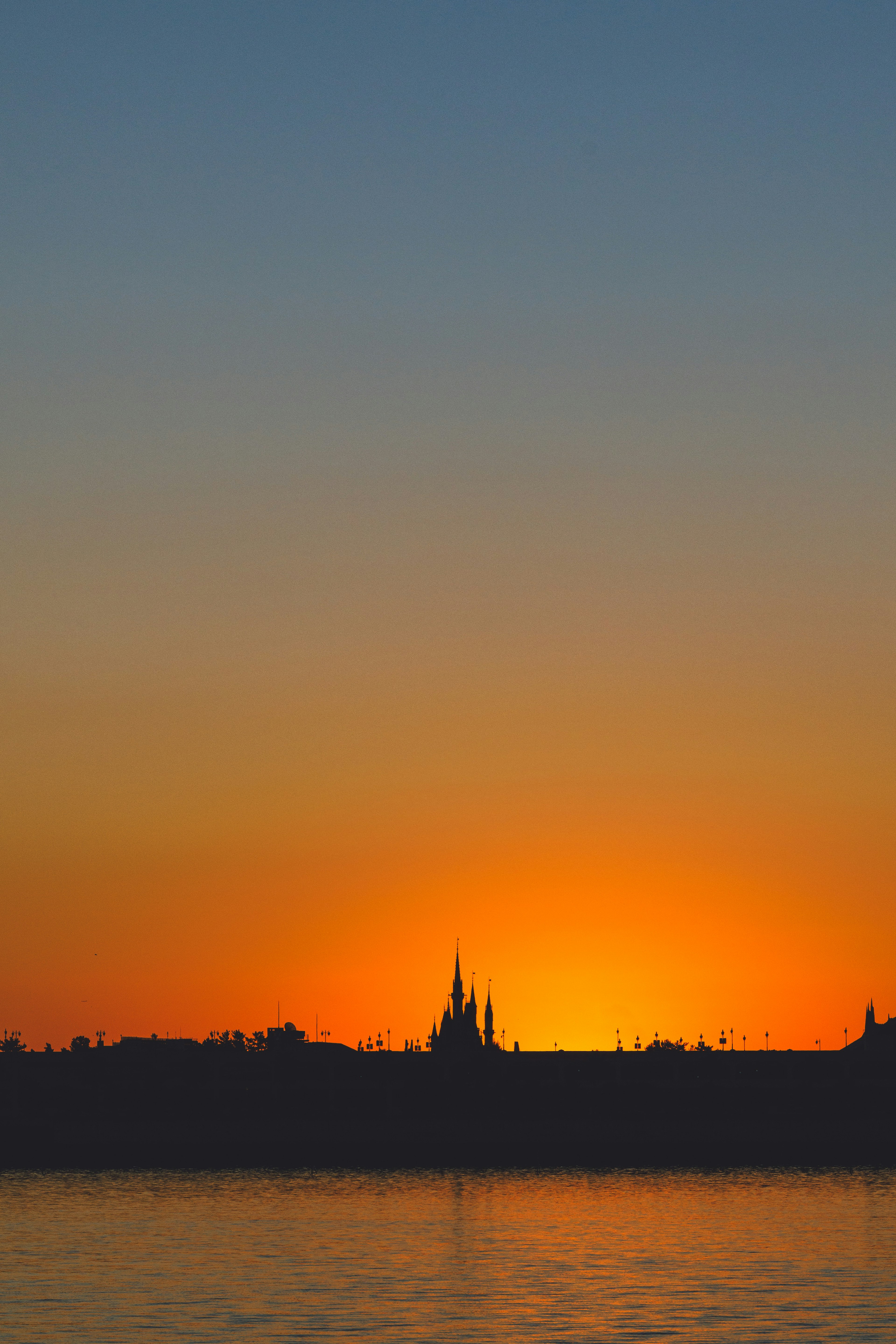 Bellissima silhouette di uno skyline contro un tramonto arancione che si riflette sull'acqua