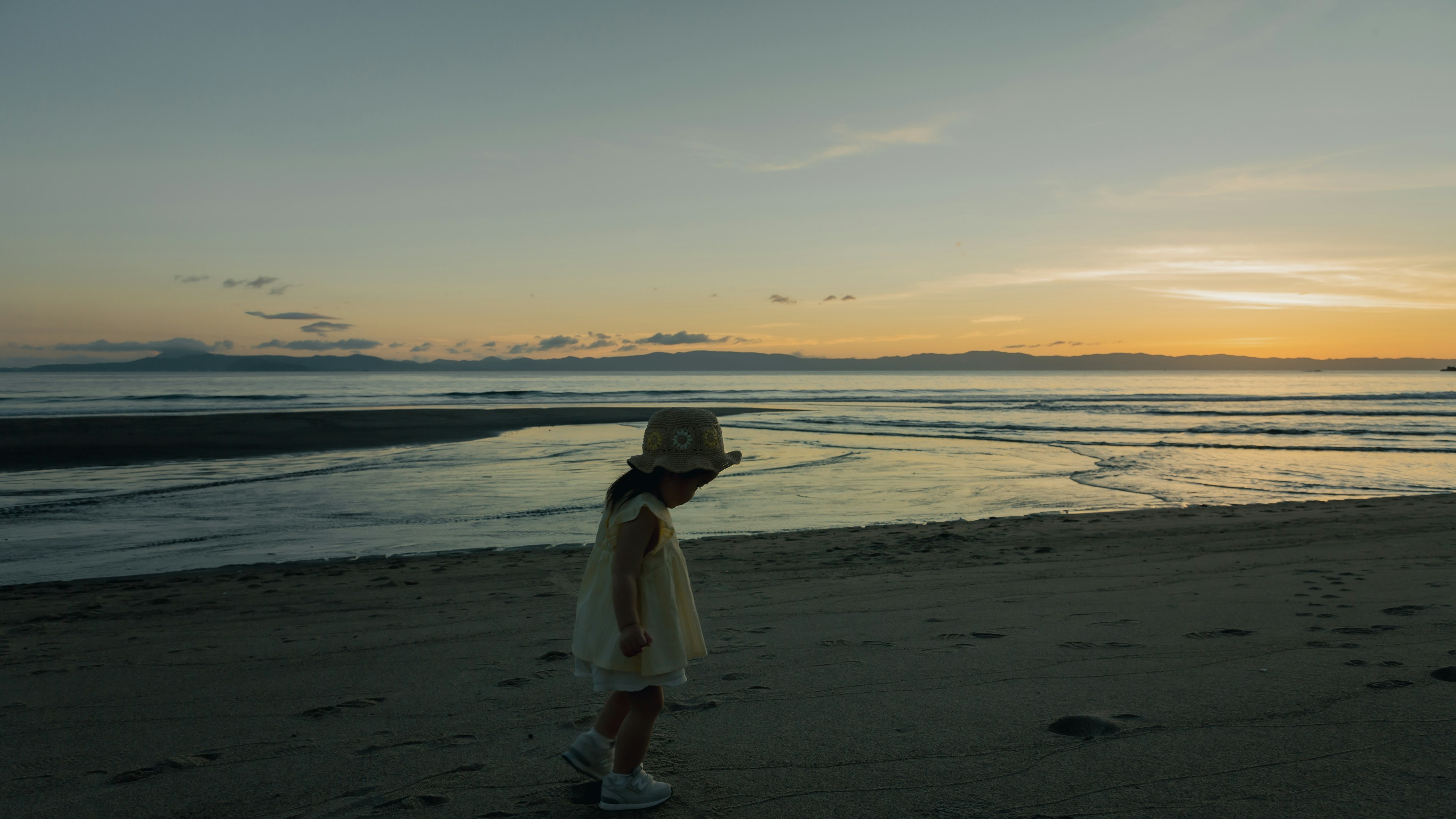 海辺を歩く子供のシルエットと夕焼けの風景