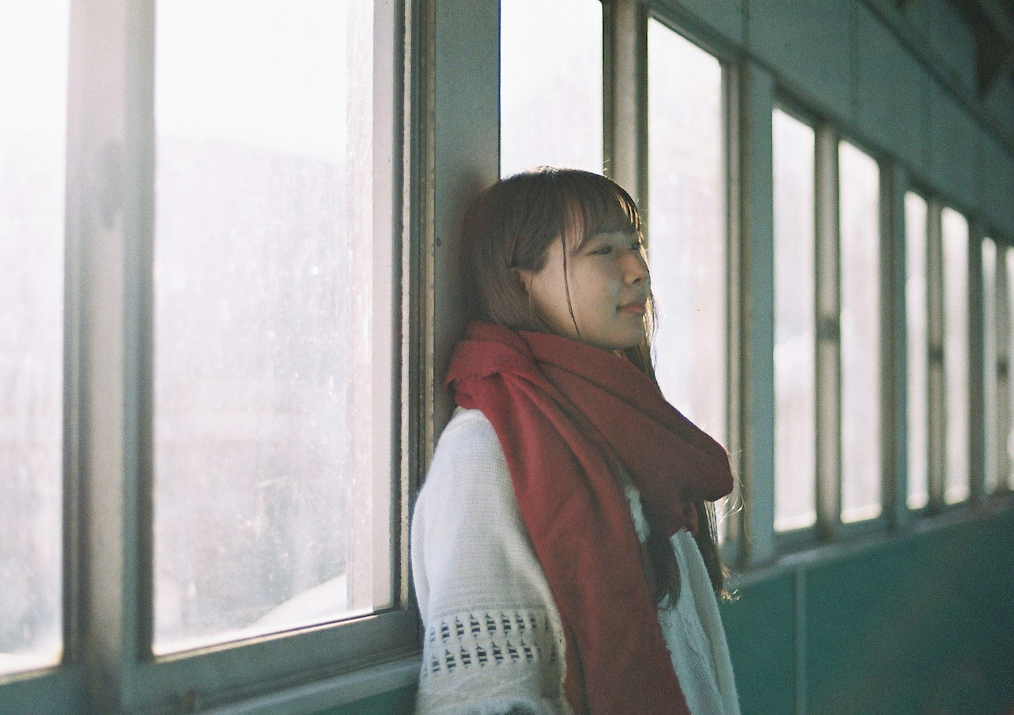 Woman leaning against a window wearing a red scarf with a calm expression