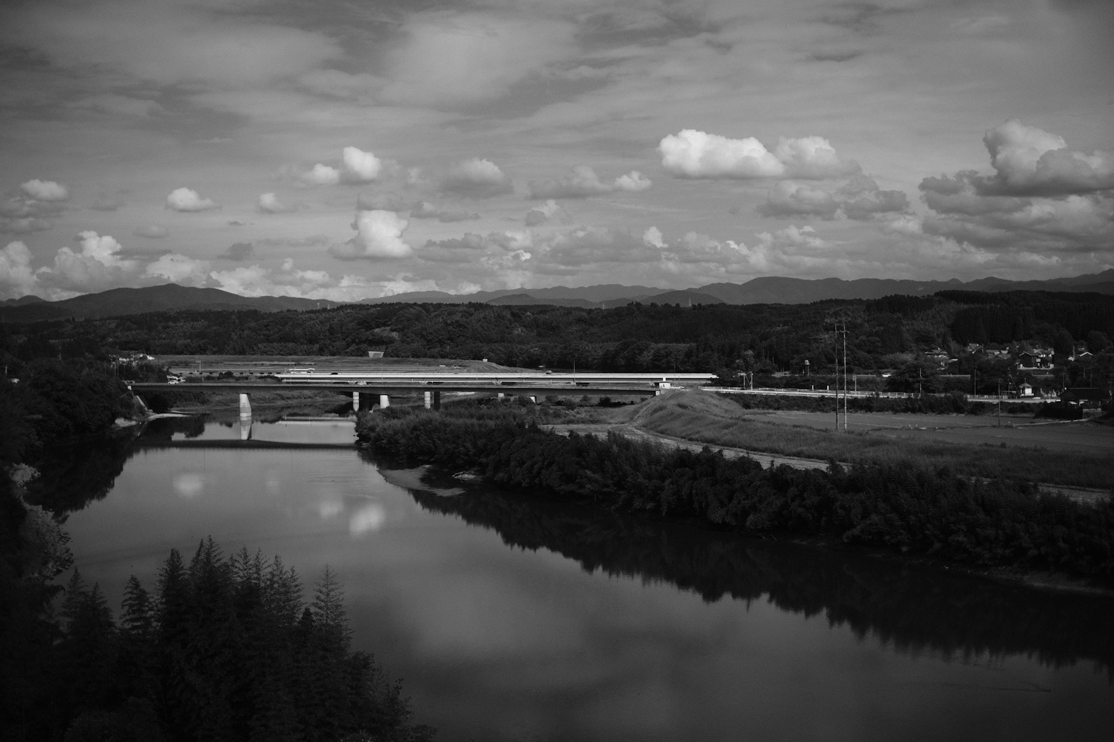 Schwarzweiß-Landschaftsfoto mit einem Fluss und einer Brücke