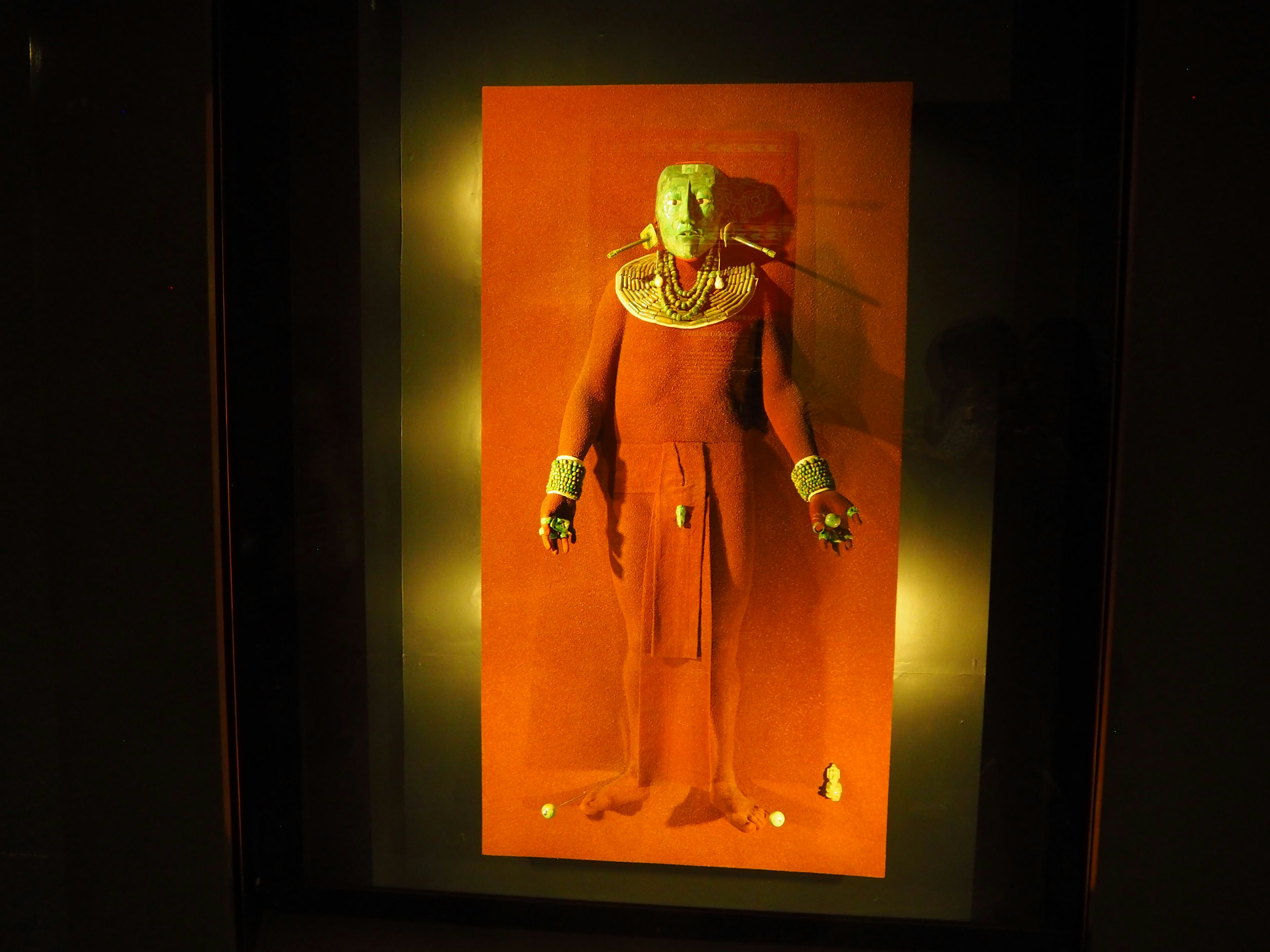 Ancient statue displayed against a red background wearing ornate headpiece