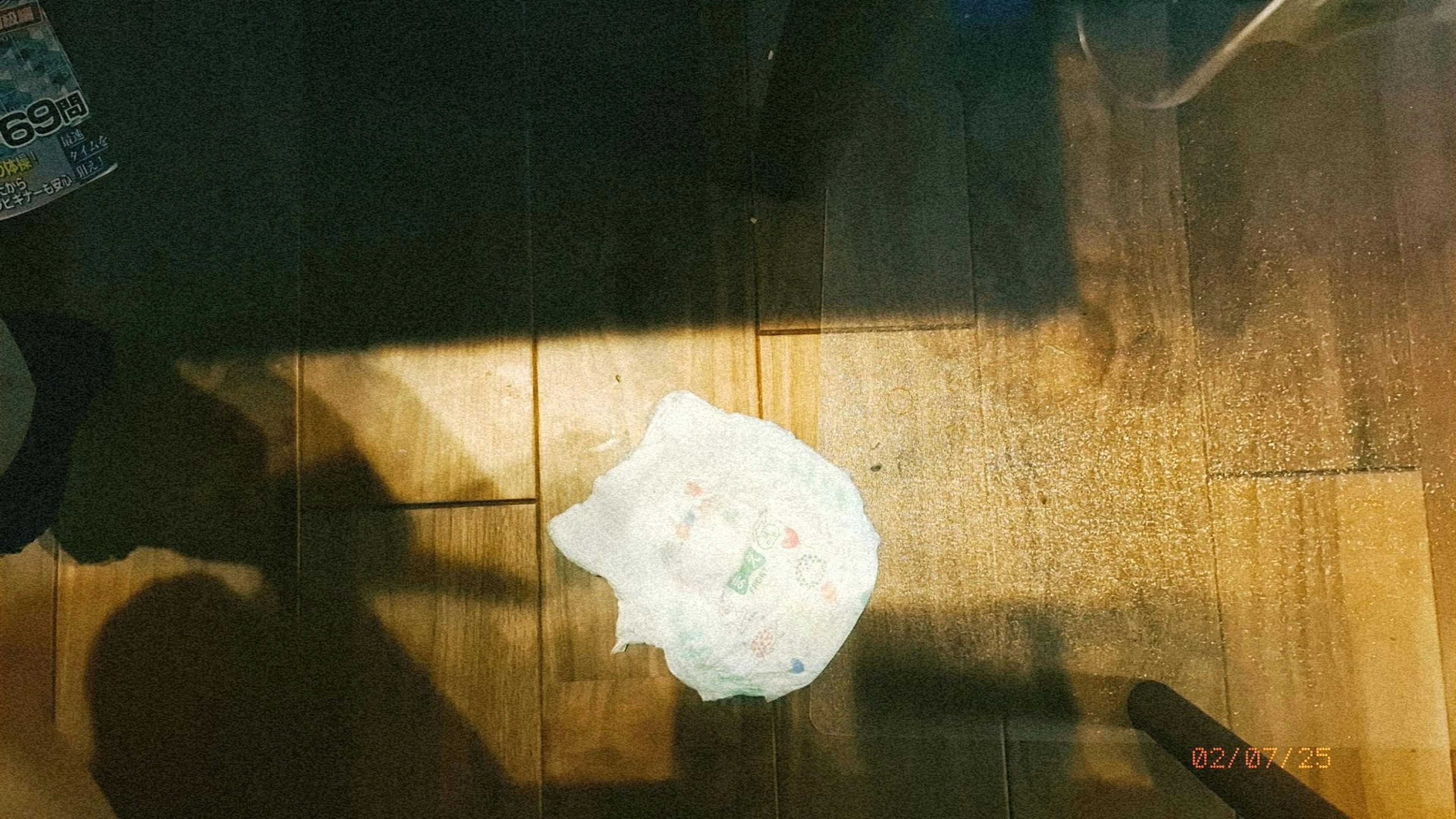 A white cloth-like object on wooden floor under bright light