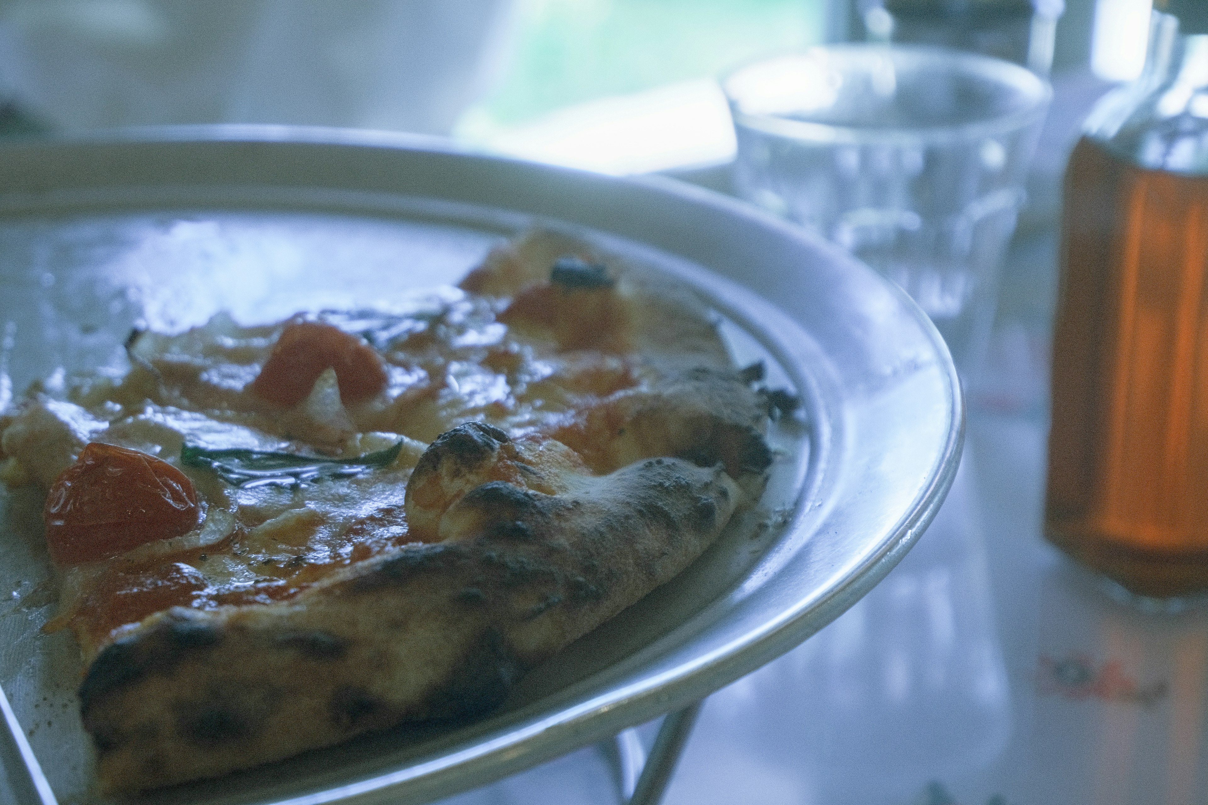 Una rebanada de pizza en un plato con tomates y un vaso de bebida