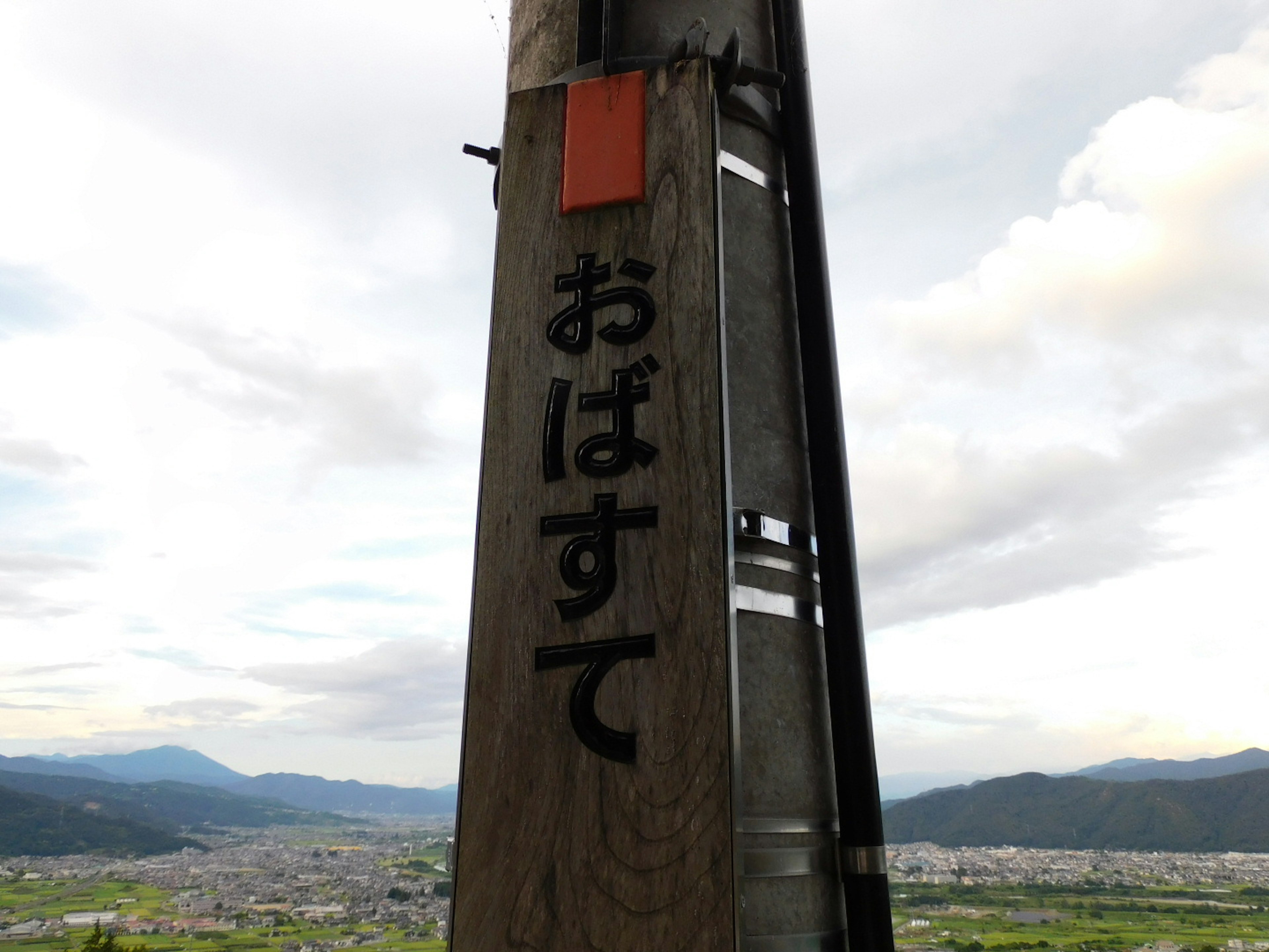 Holzpfeiler mit den Zeichen 'おばすて' und einer malerischen Kulisse