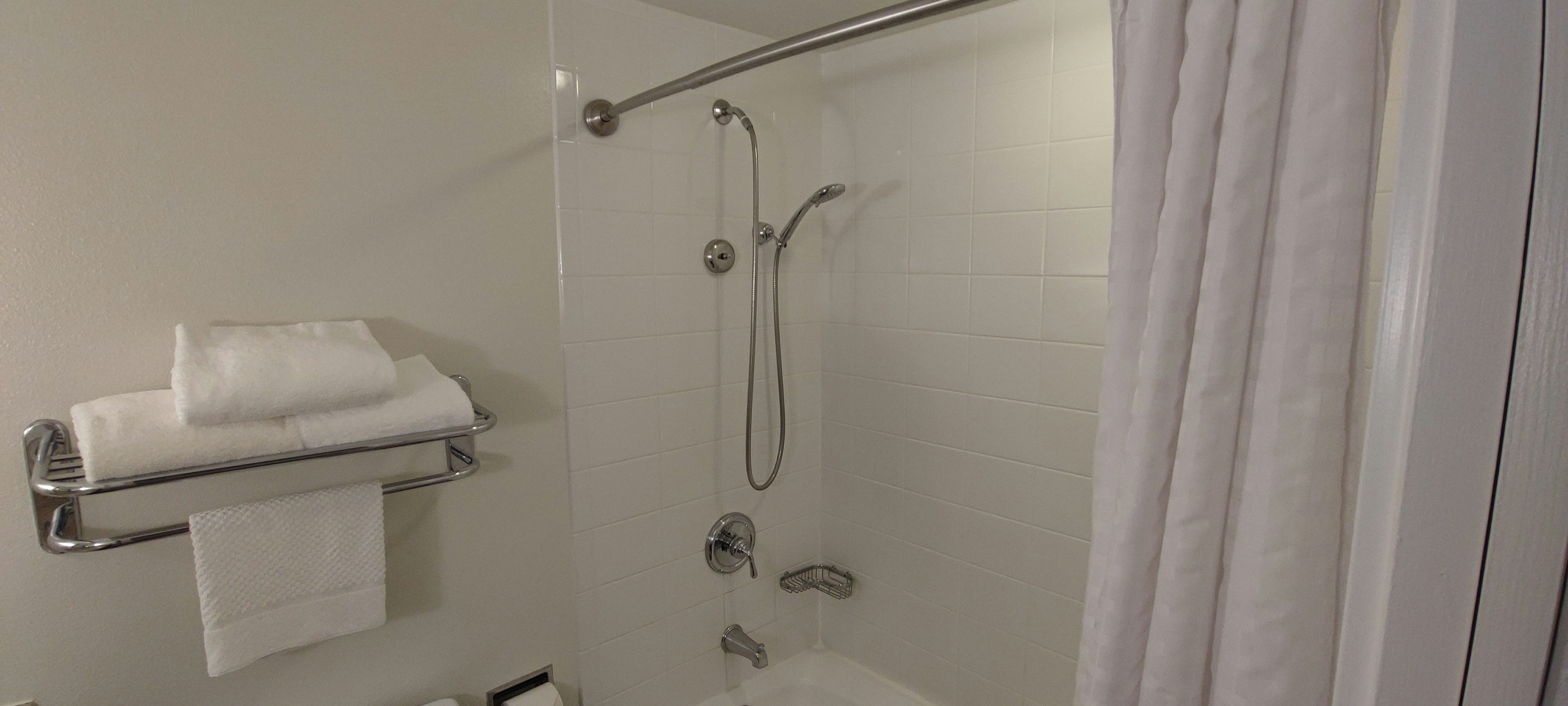 Clean bathroom shower area with towels on a shelf