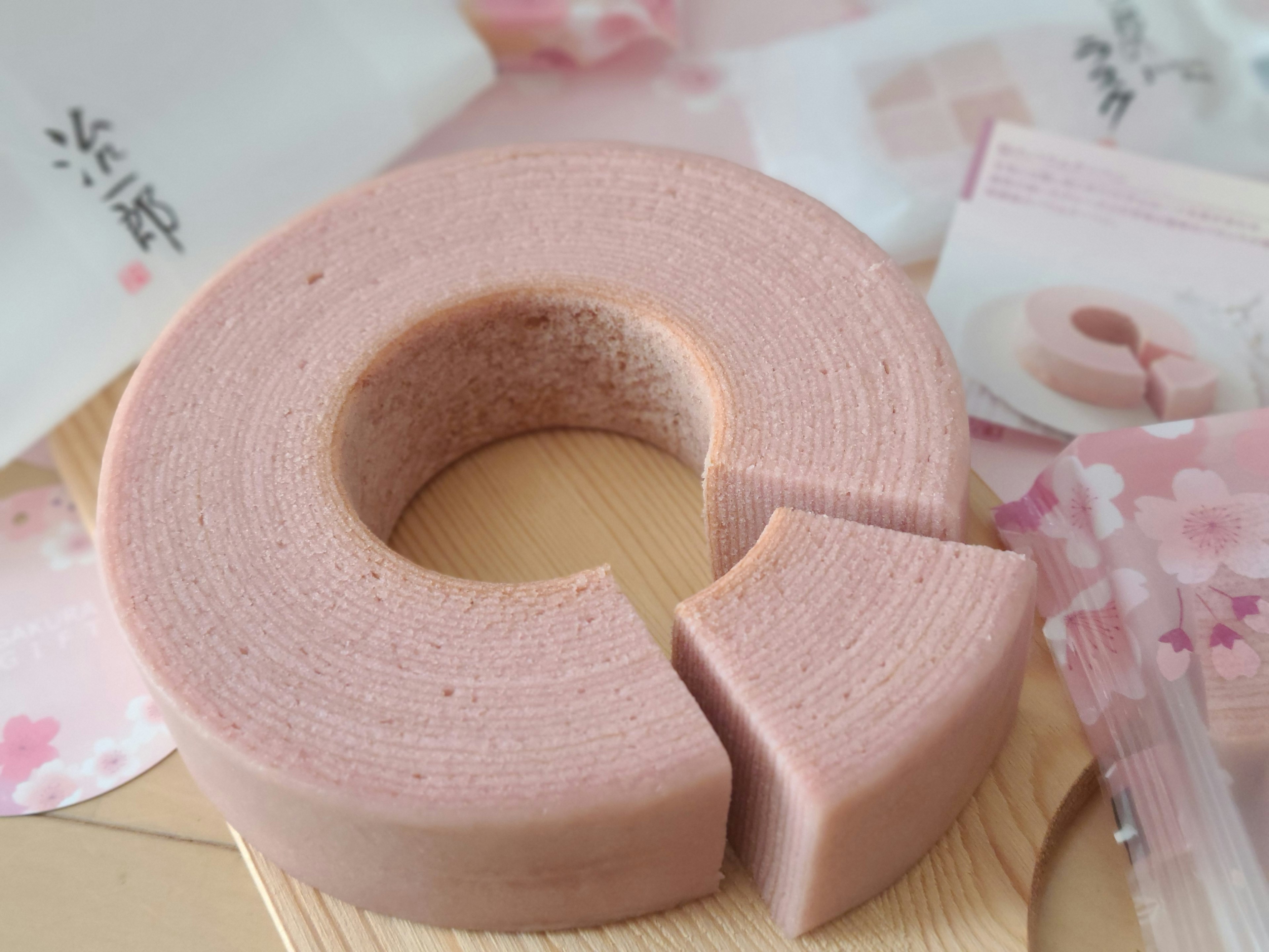 Il Baumkuchen rosa è posato su un piatto di legno con una porzione tagliata visibile