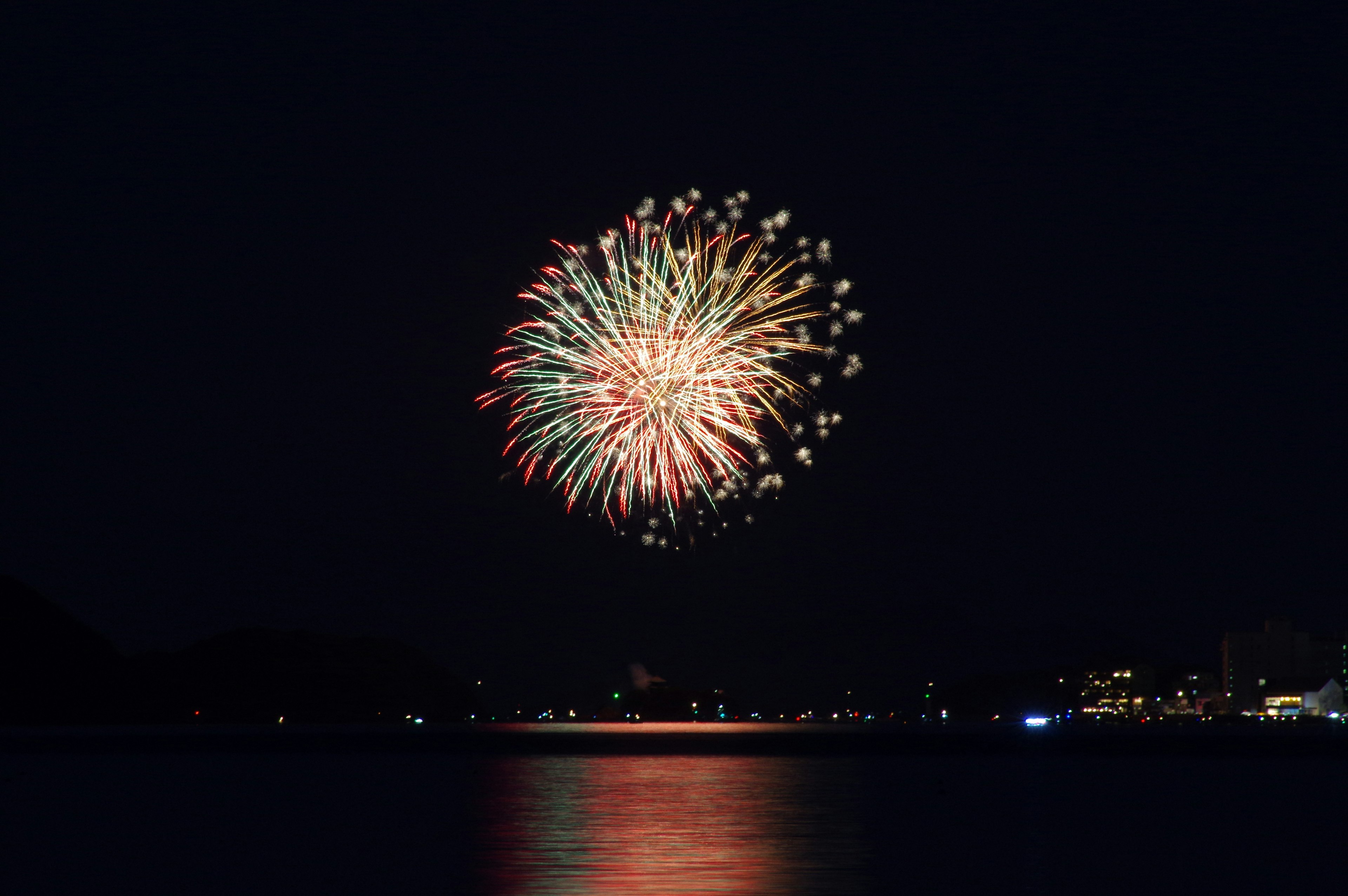 Fuegos artificiales coloridos estallando en el cielo nocturno reflejándose en el agua