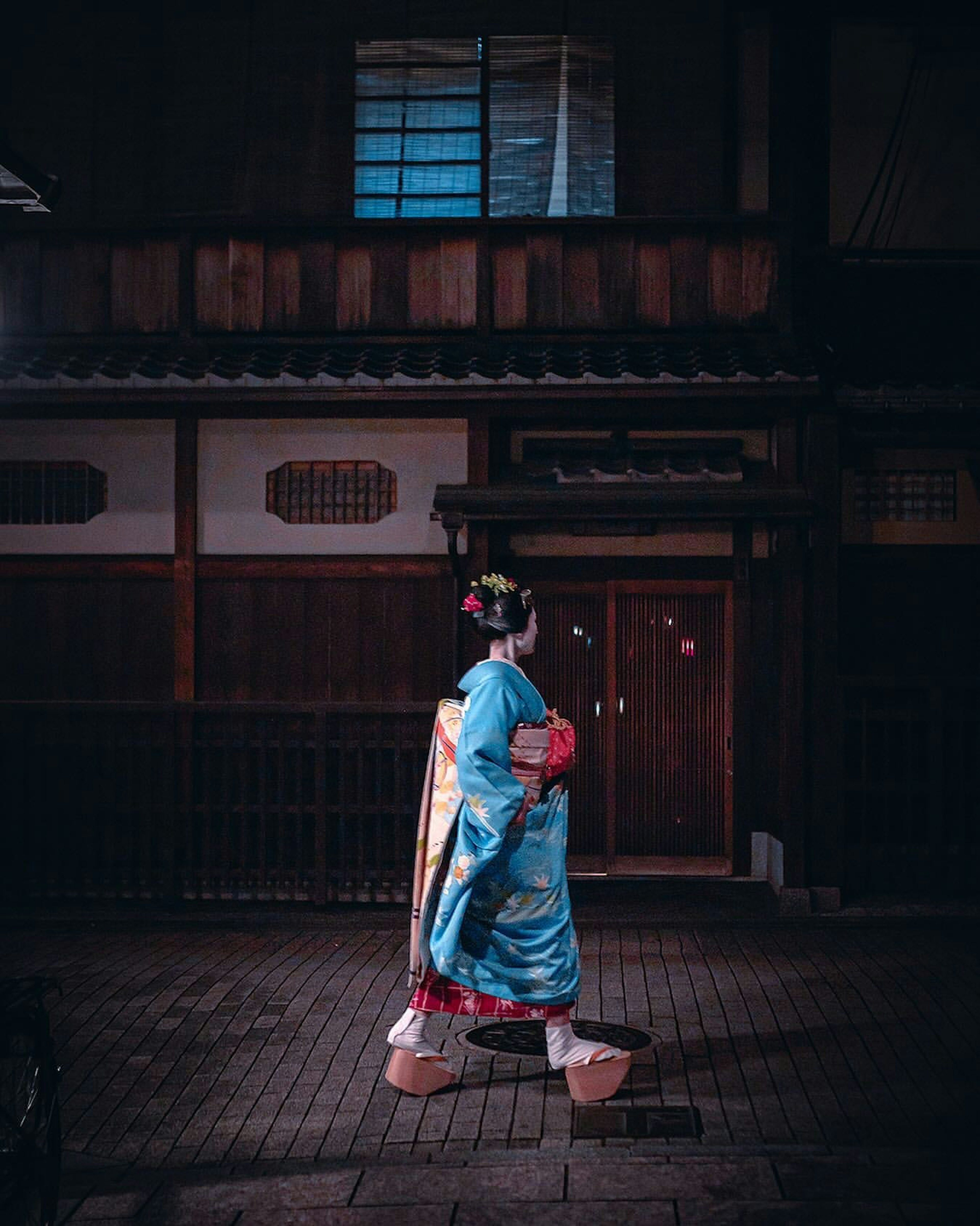 Frau im Kimono, die nachts neben einem traditionellen japanischen Haus geht