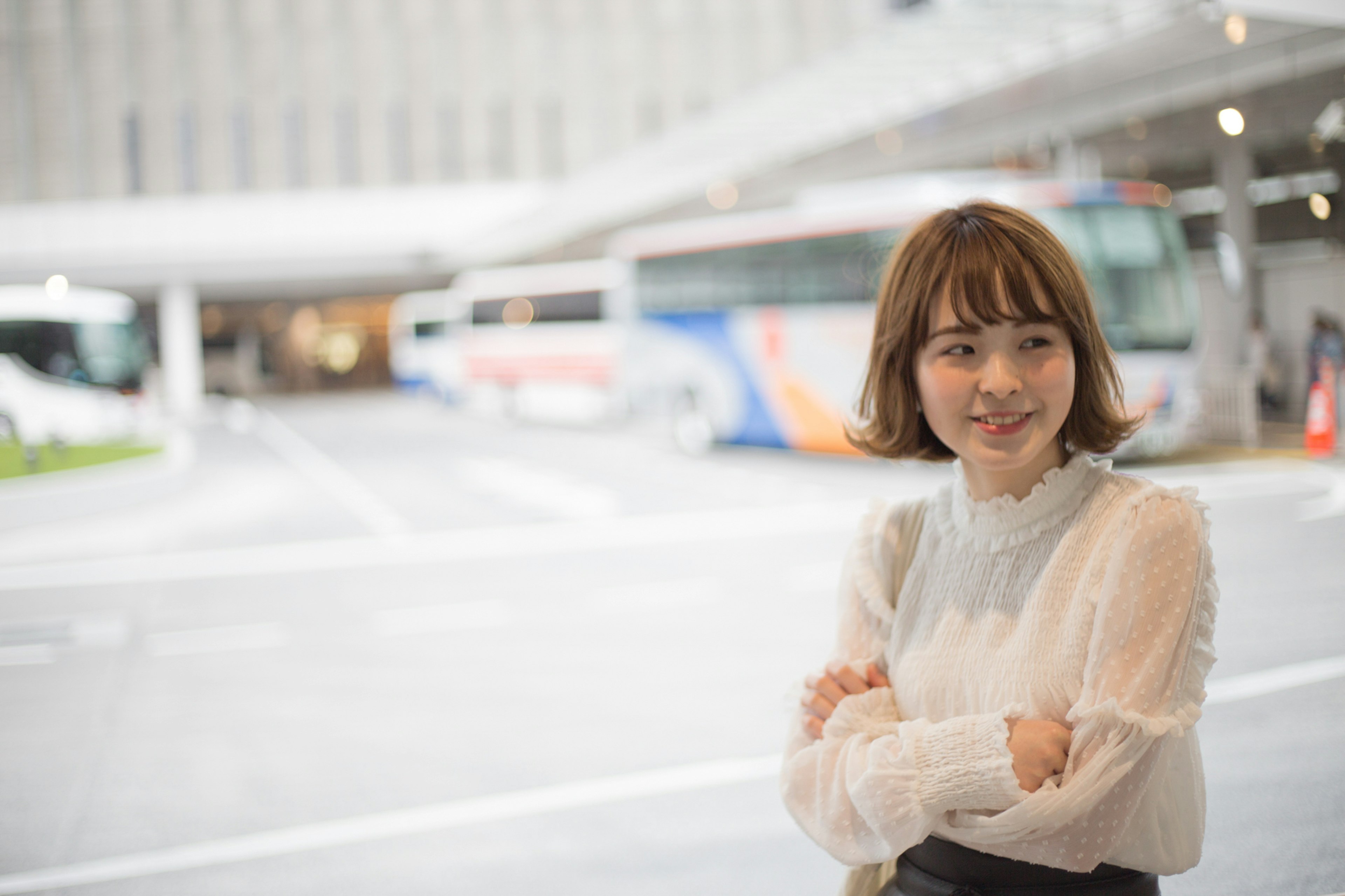 A woman smiling with arms crossed in front of a bus terminal