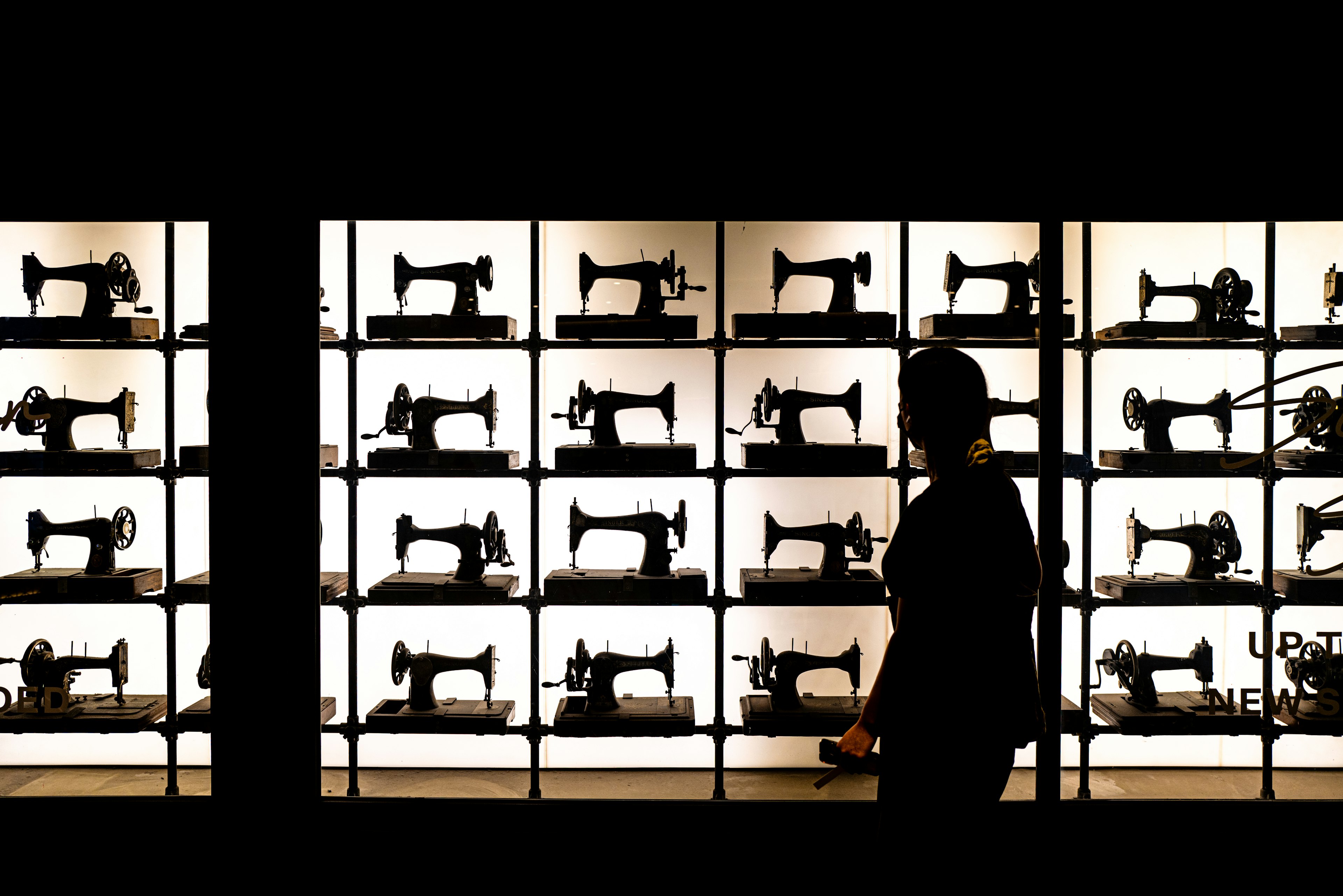 Silueta de una persona observando una fila de máquinas de coser vintage