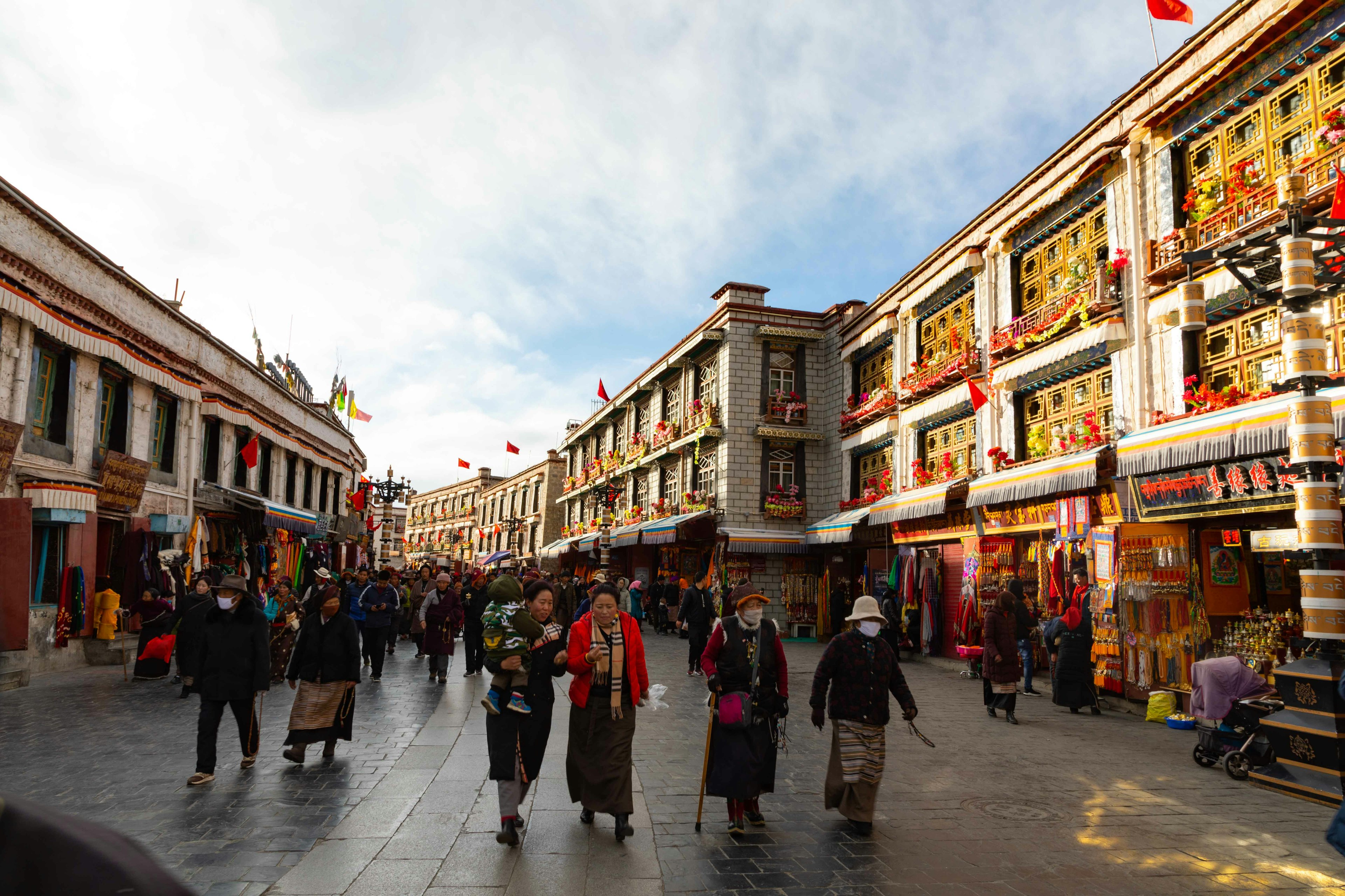 Orang-orang berjalan di jalanan Tibet dengan toko-toko berwarna-warni