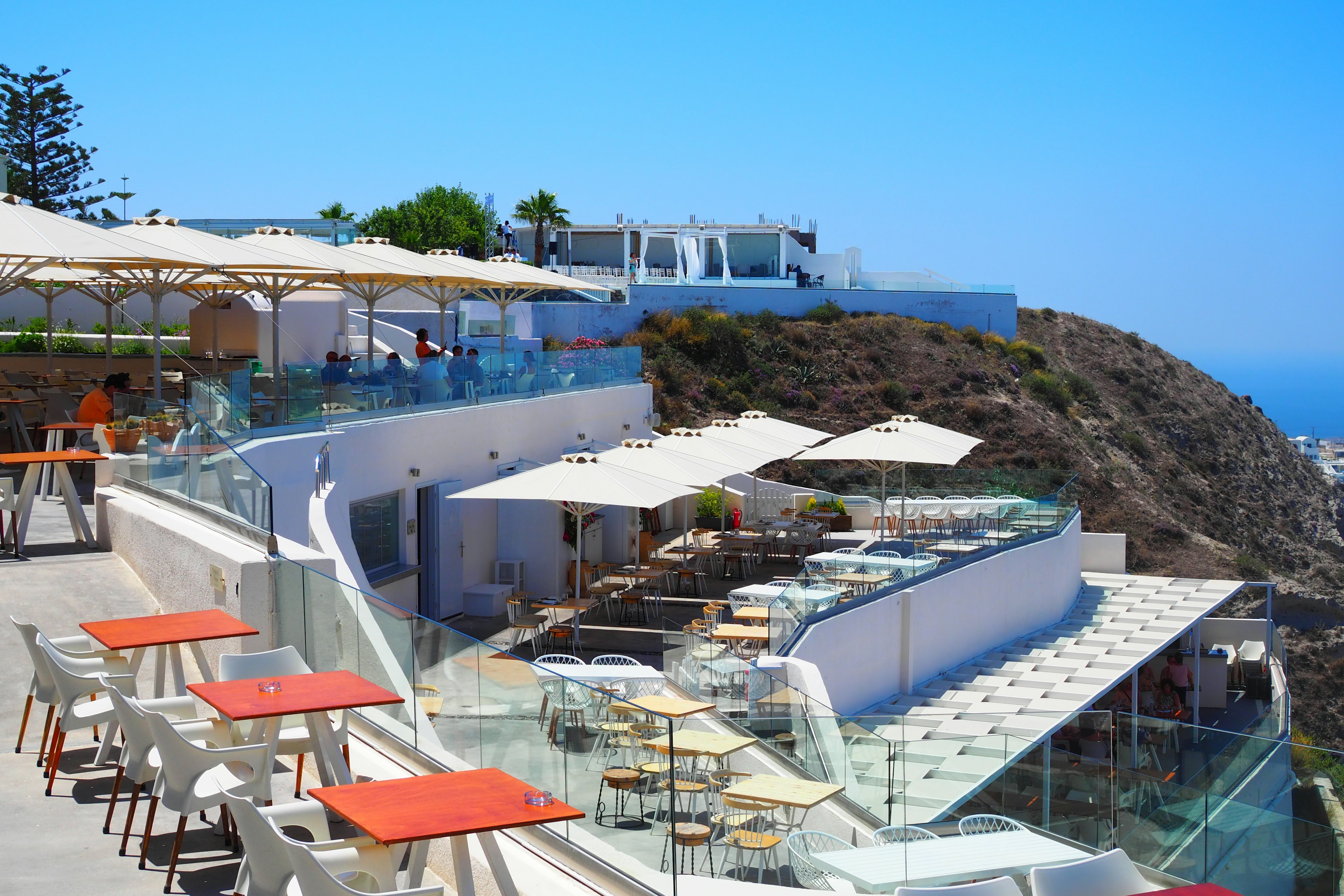 Terrace of a seaside restaurant with white chairs and tables under a blue sky