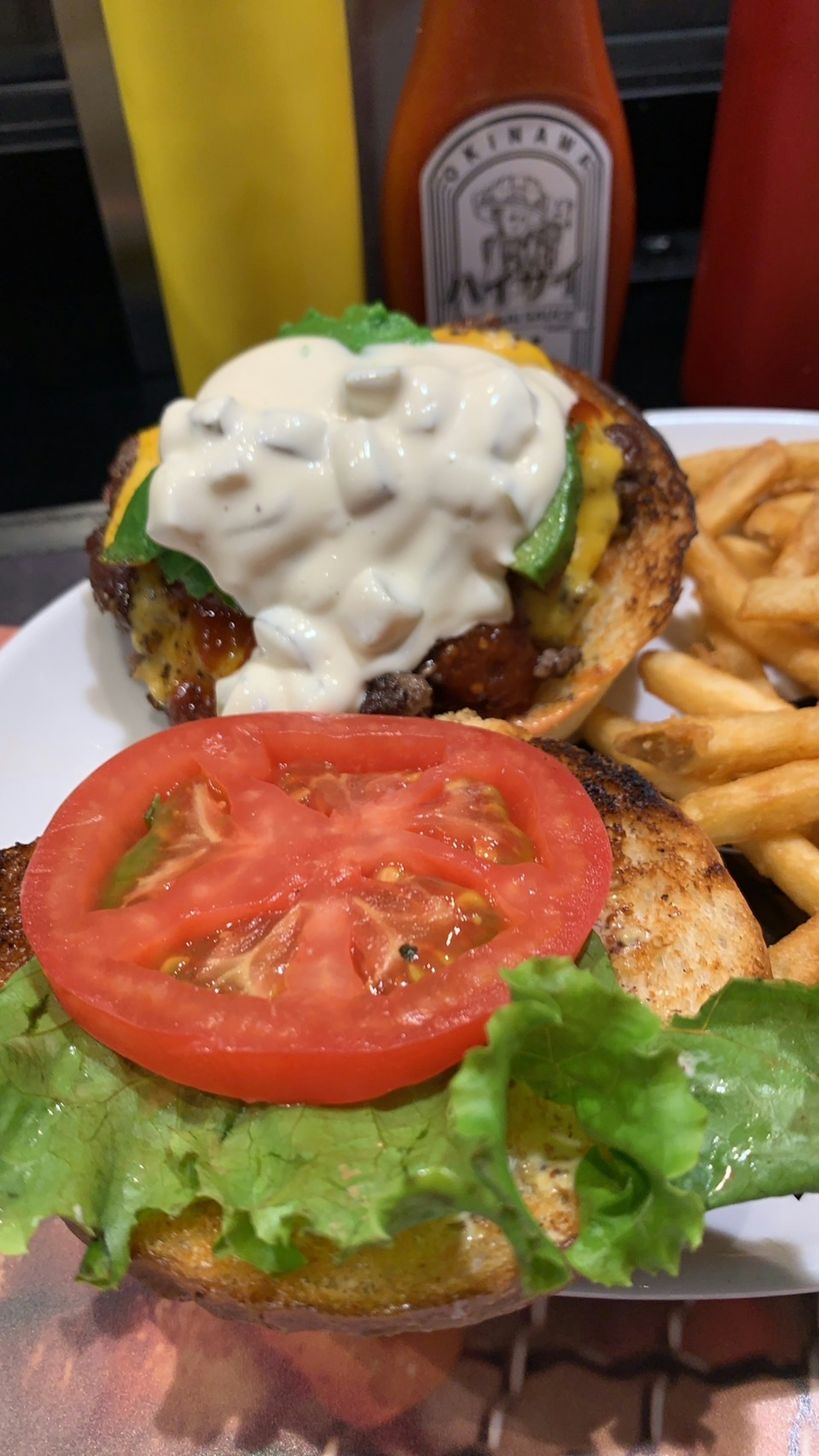 Plato de hamburguesa con lechuga y tomate mayonesa y guarnición de aguacate servido con papas fritas