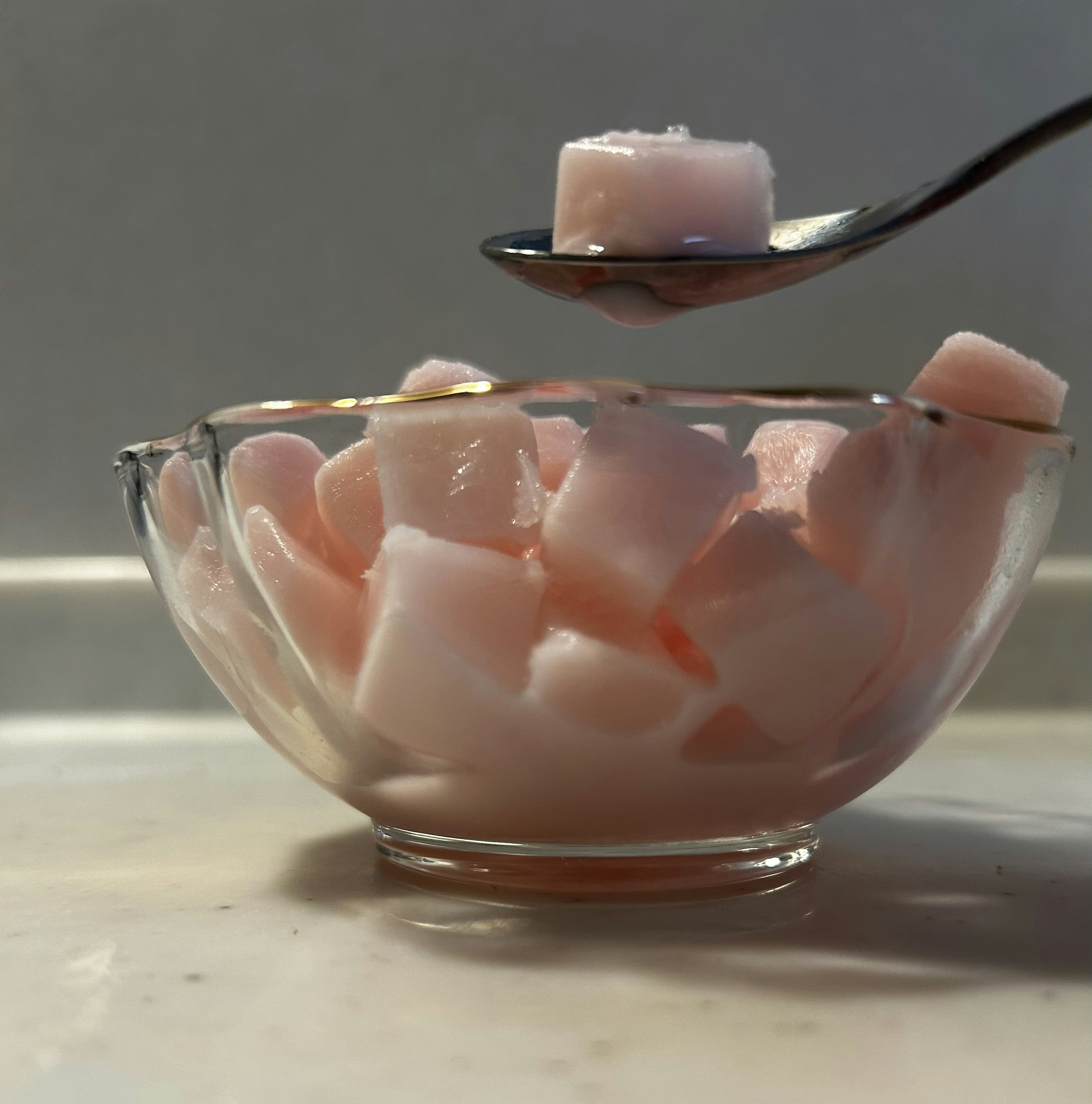 Pink cube-shaped sugar pieces in a clear glass bowl with a spoon