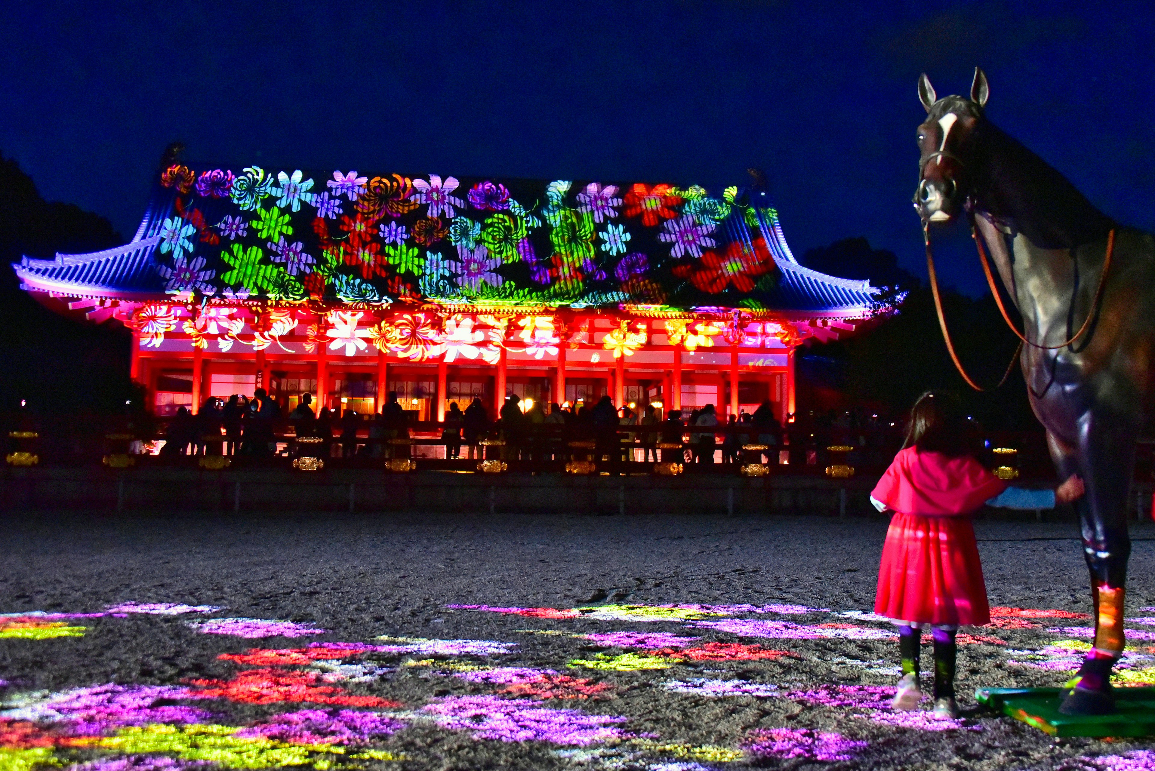 Seorang gadis berpakaian pink berdiri di depan bangunan tradisional yang diterangi pada malam hari