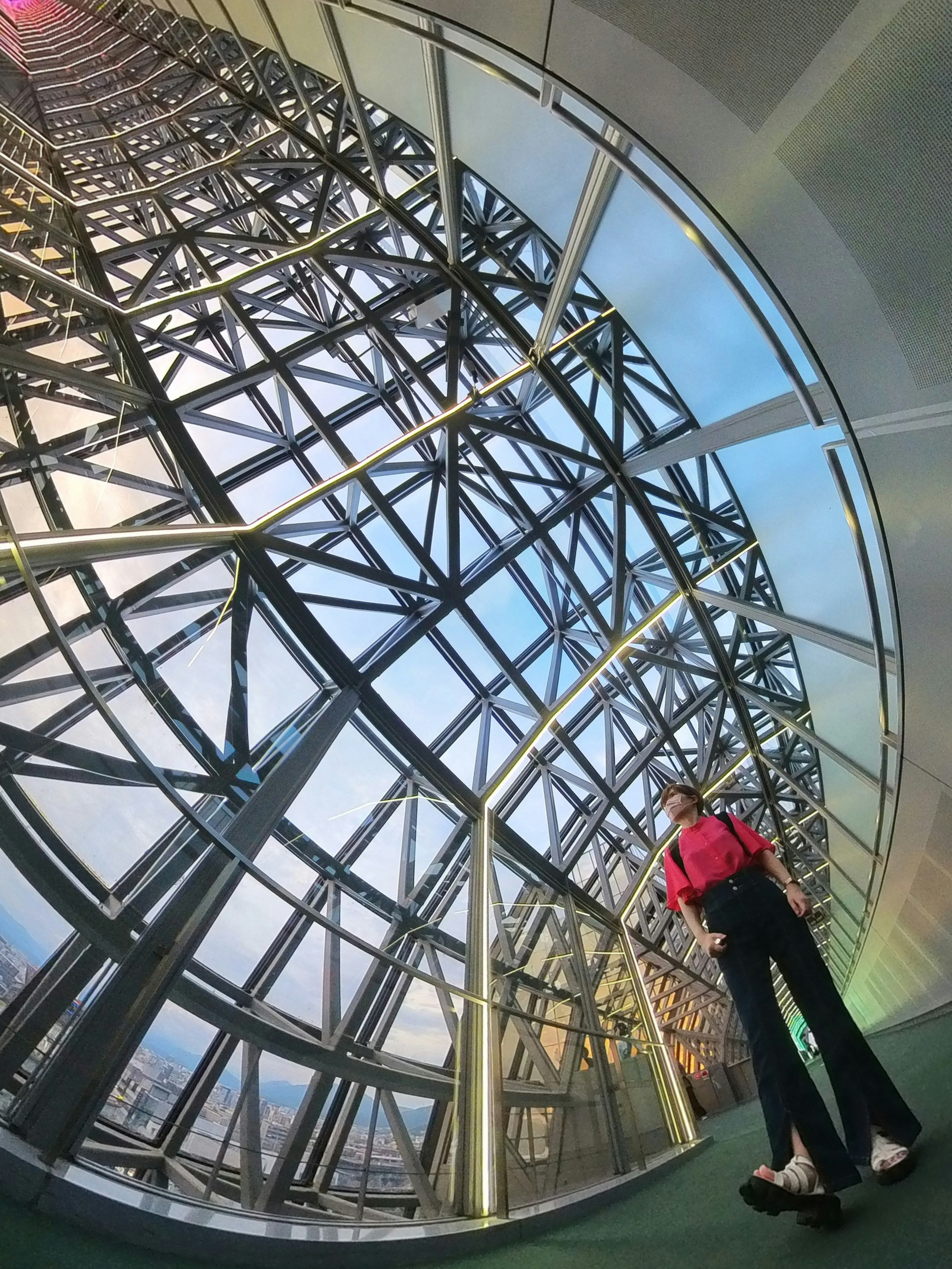 Une femme en haut rouge et pantalon noir se tient à l'intérieur d'une structure en verre