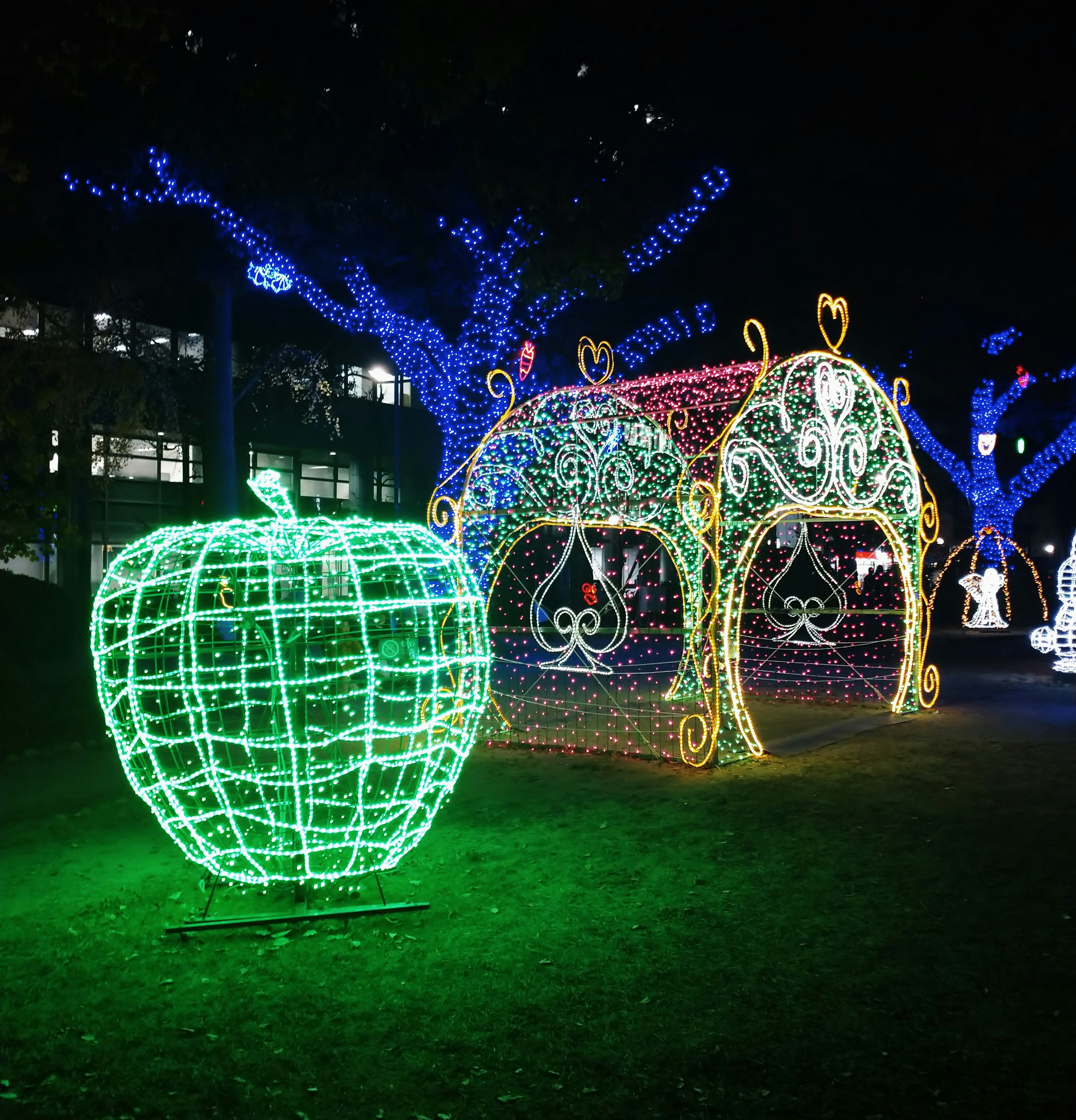 夜の公園に輝く緑のリンゴ型のイルミネーションとカラフルな装飾の小屋