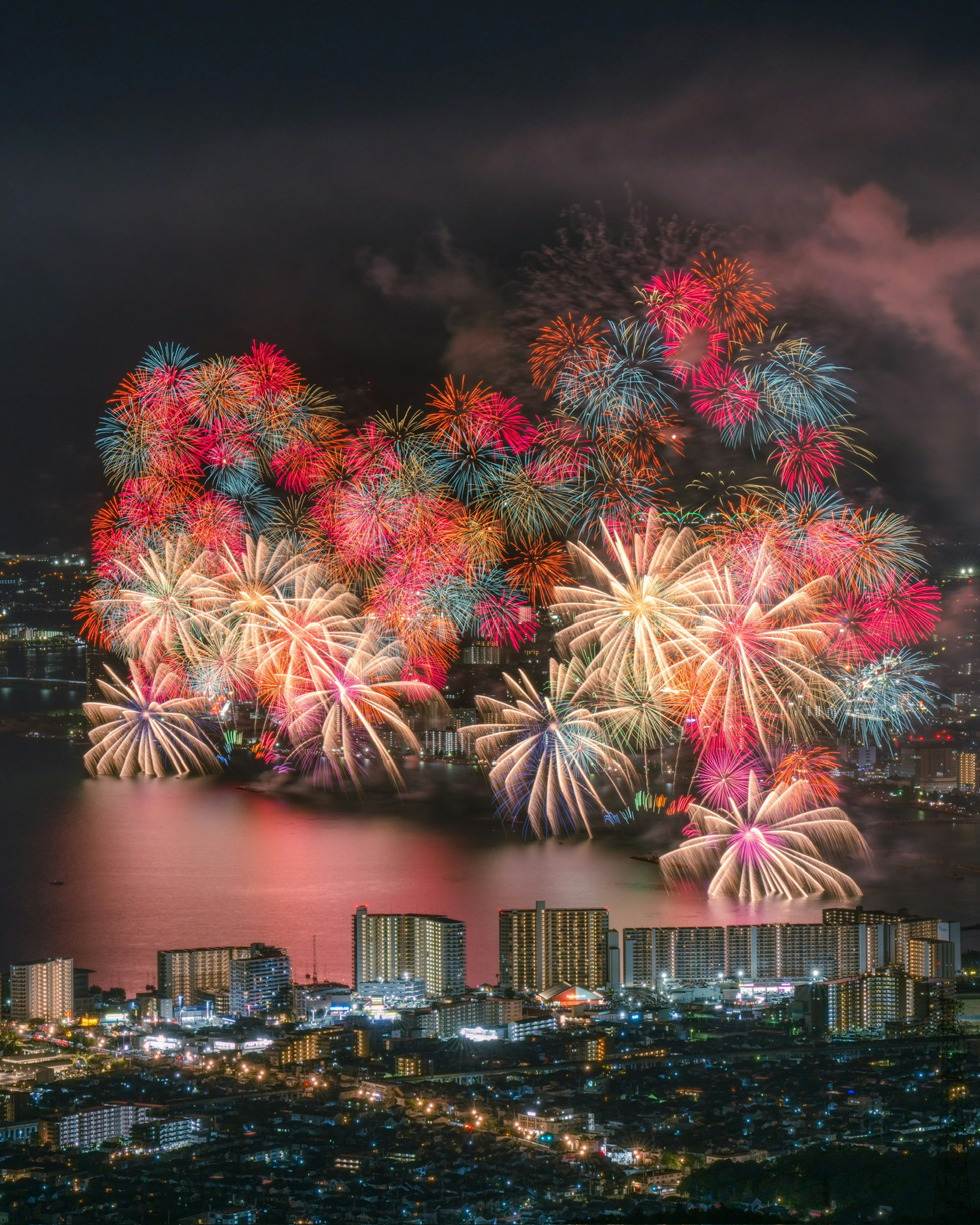 Espectáculo de fuegos artificiales coloridos sobre un lago de noche con luces de la ciudad abajo