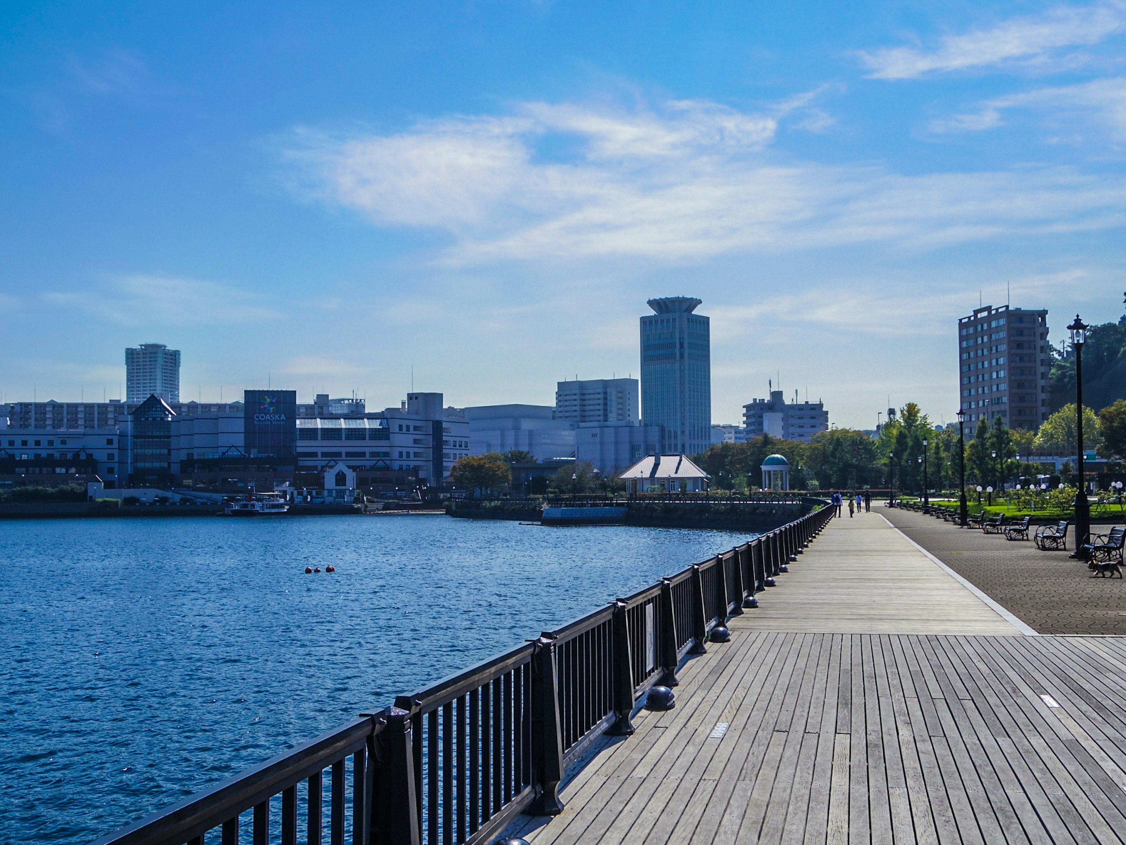 Paseo frente al agua con edificios modernos bajo un cielo azul claro