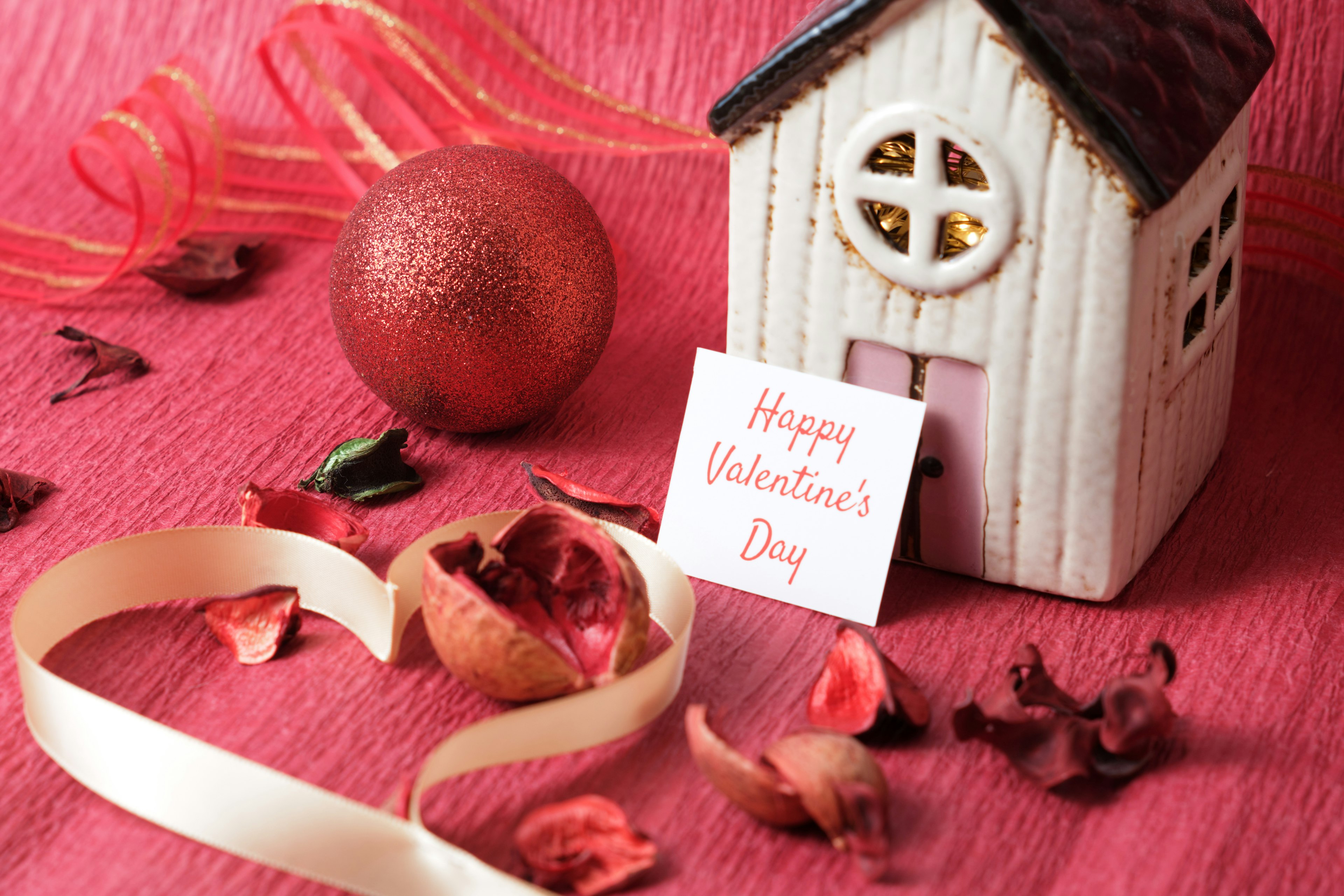 Decorazione di San Valentino con un piccolo oggetto a forma di casa nastro rosso e petali sparsi