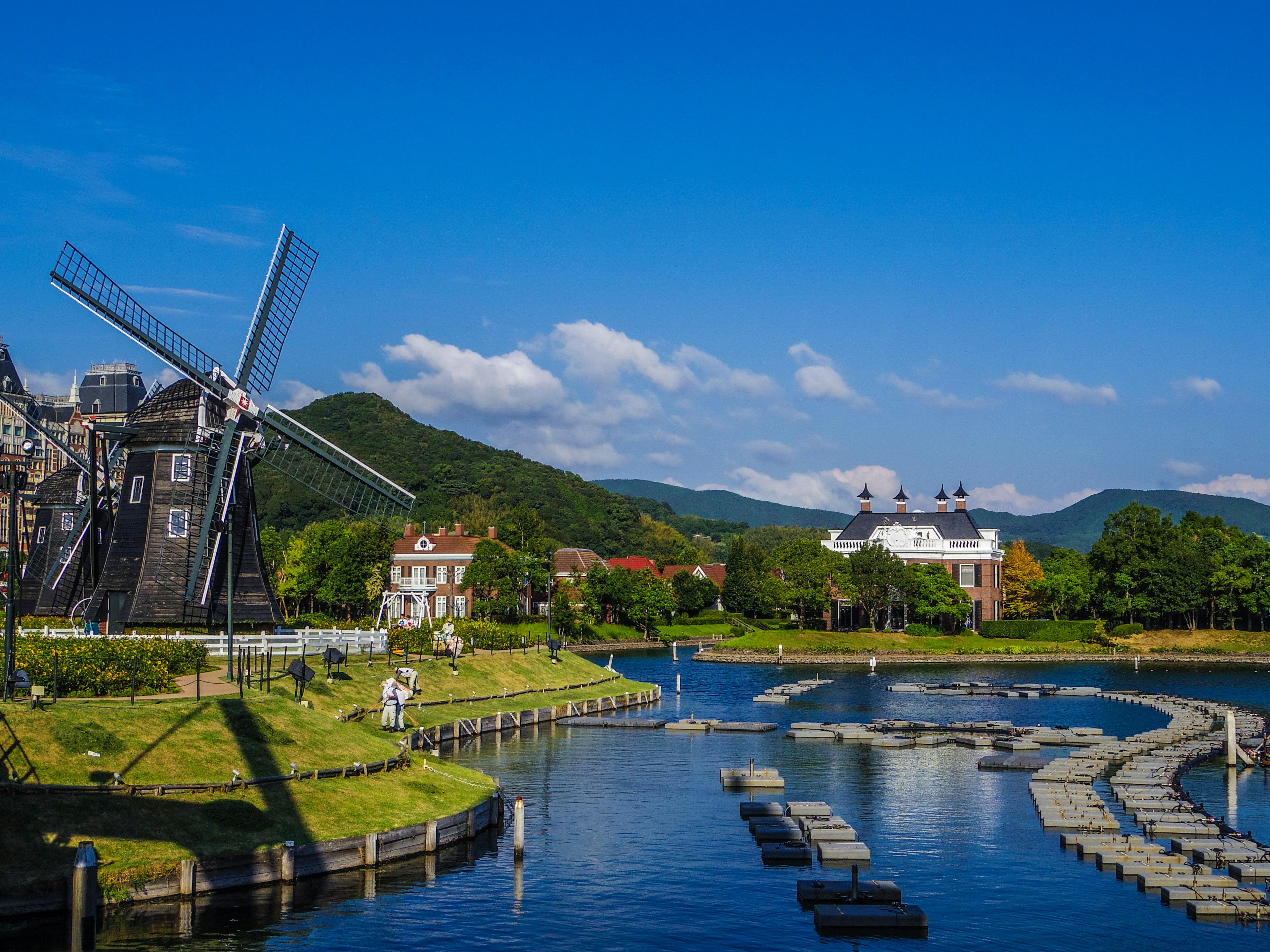 Malersicher Blick auf eine Windmühle an einem Fluss üppiges grünes Gras unter einem klaren blauen Himmel